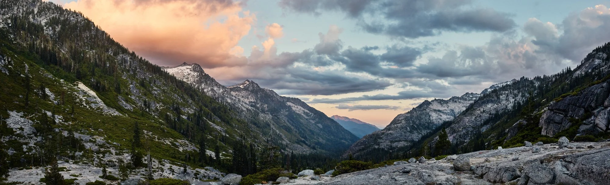 Scenic mountain valley with snow-capped peaks in the Trinity Alps northern California, green forested slopes, and a partly cloudy sky during sunset.