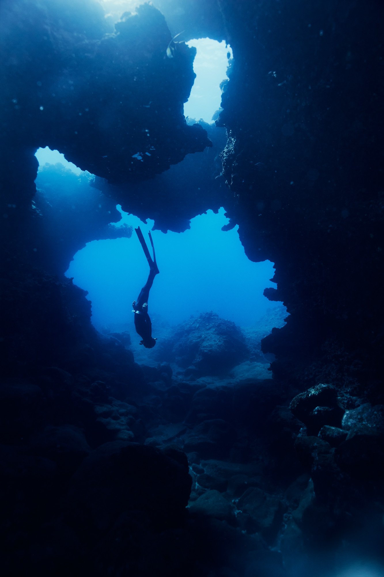 A diver exploring an underwater cave with interesting rock formations and clear blue water. Cathedrals off of Sharks Cove Oahu Hawaii