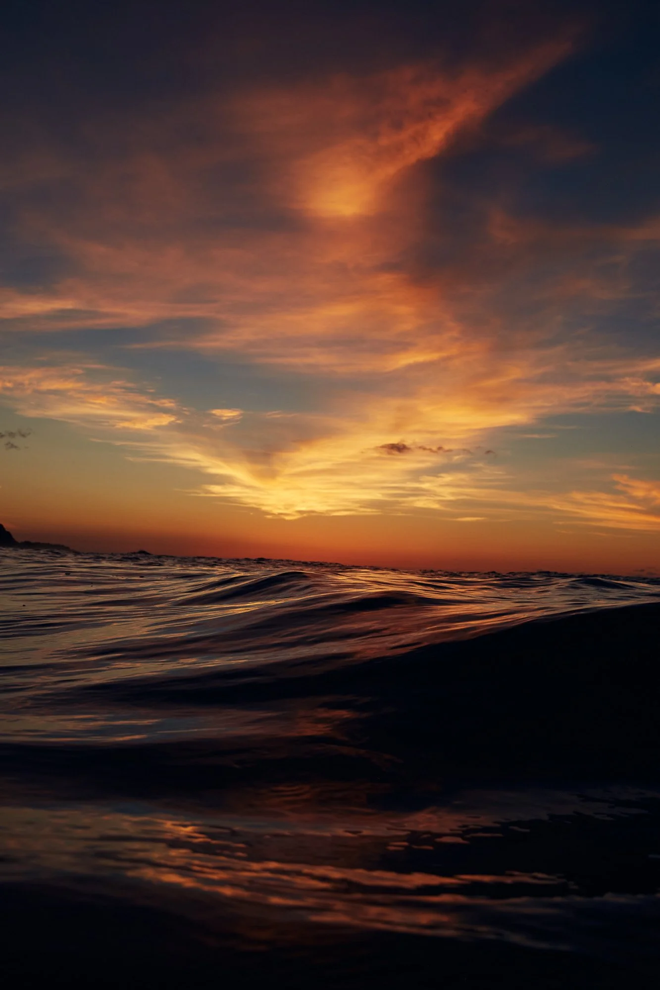 Sunset over the ocean with colorful clouds and gentle waves in the foreground.