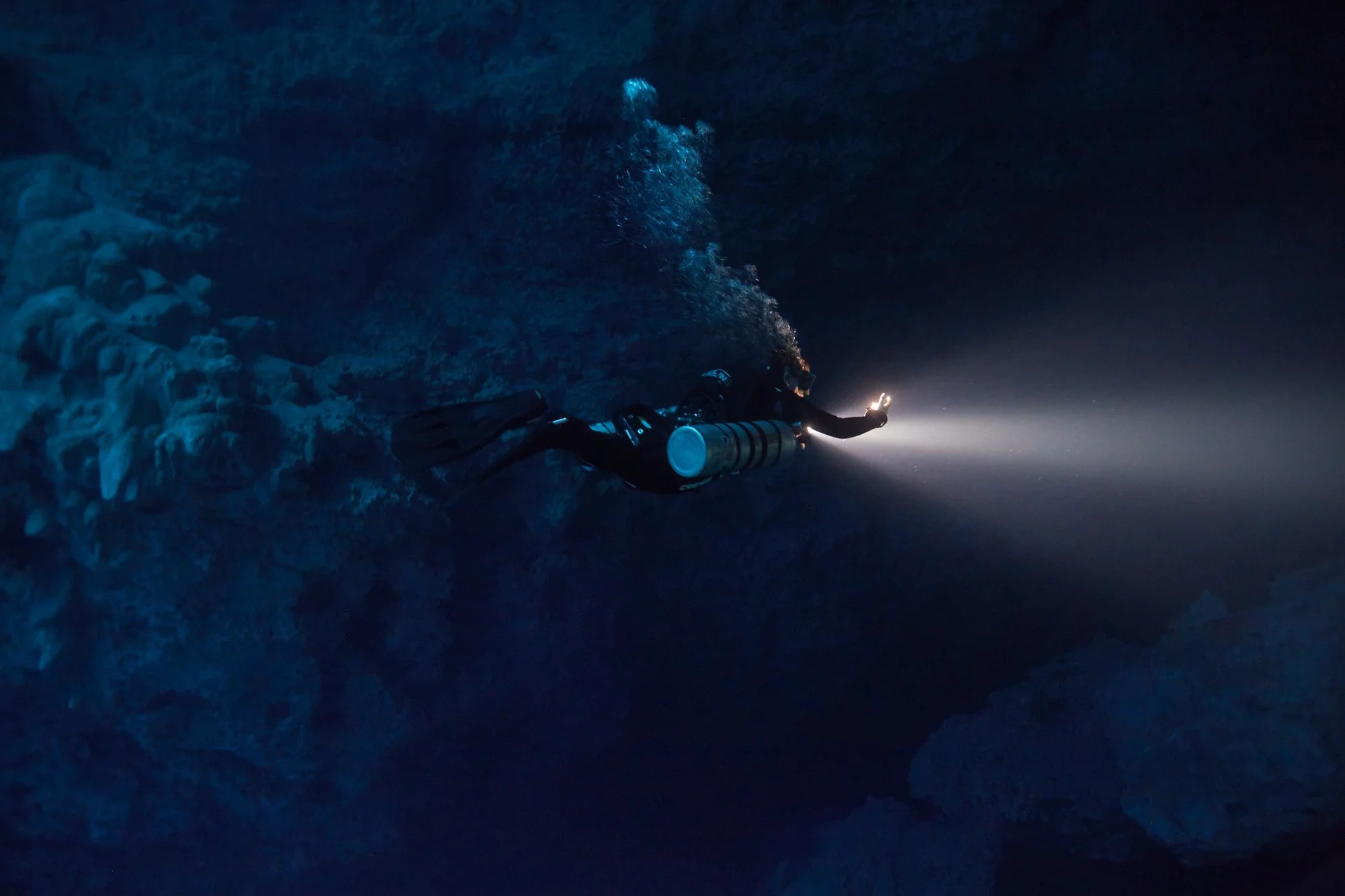 A scuba diver with a flashlight exploring an underwater cenote El Pit, near Playa del Carmen, in the Yucatan Peninsula of Mexico.