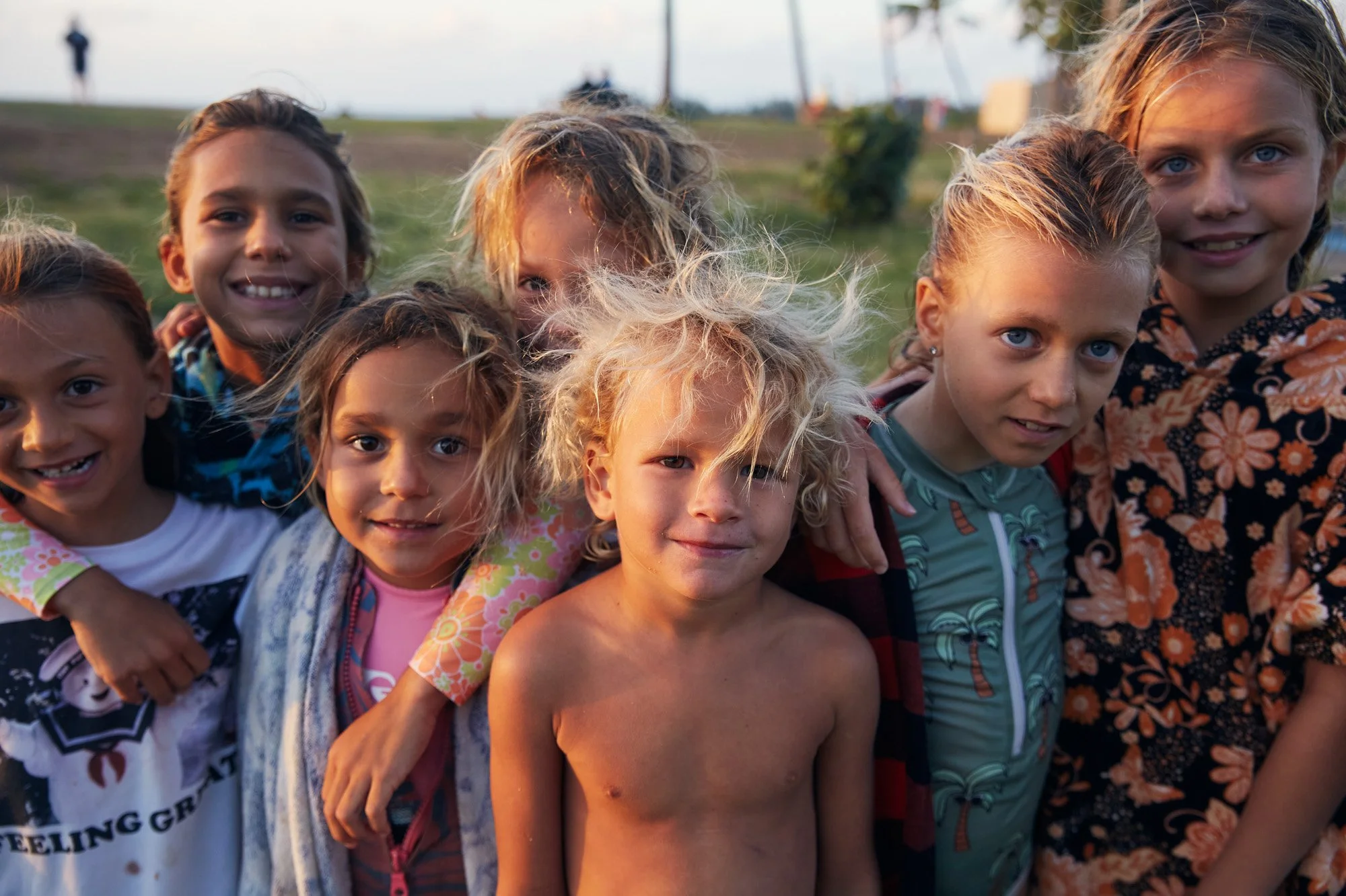 Group of children at Halweiwa Beach Park on Oahu Hawaii, smiling and posing outdoors on a grassy area during sunset.