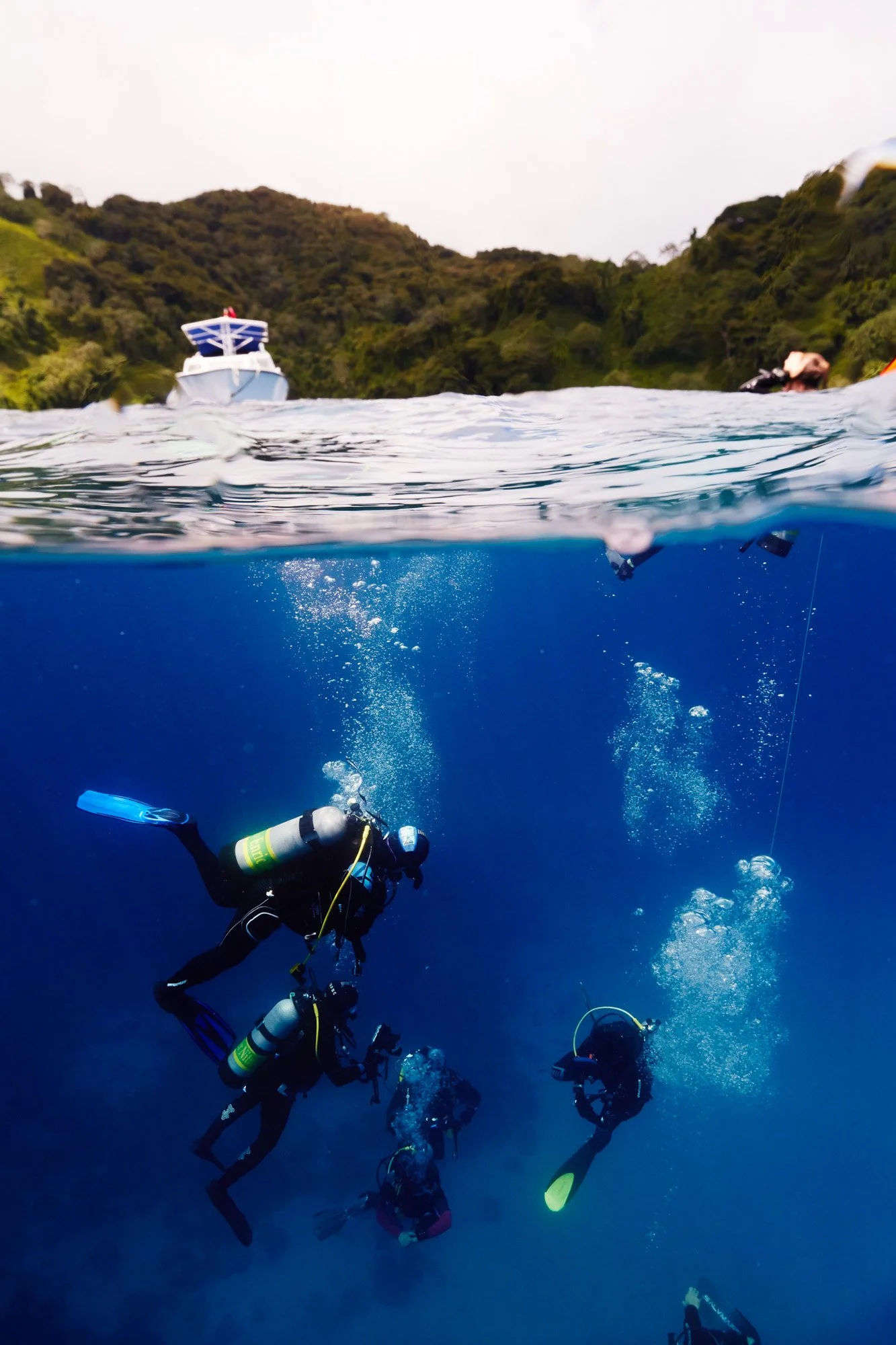 Underwater scuba divers diving in blue ocean with a boat and green island in the background of Cocos Island Costa Rica.