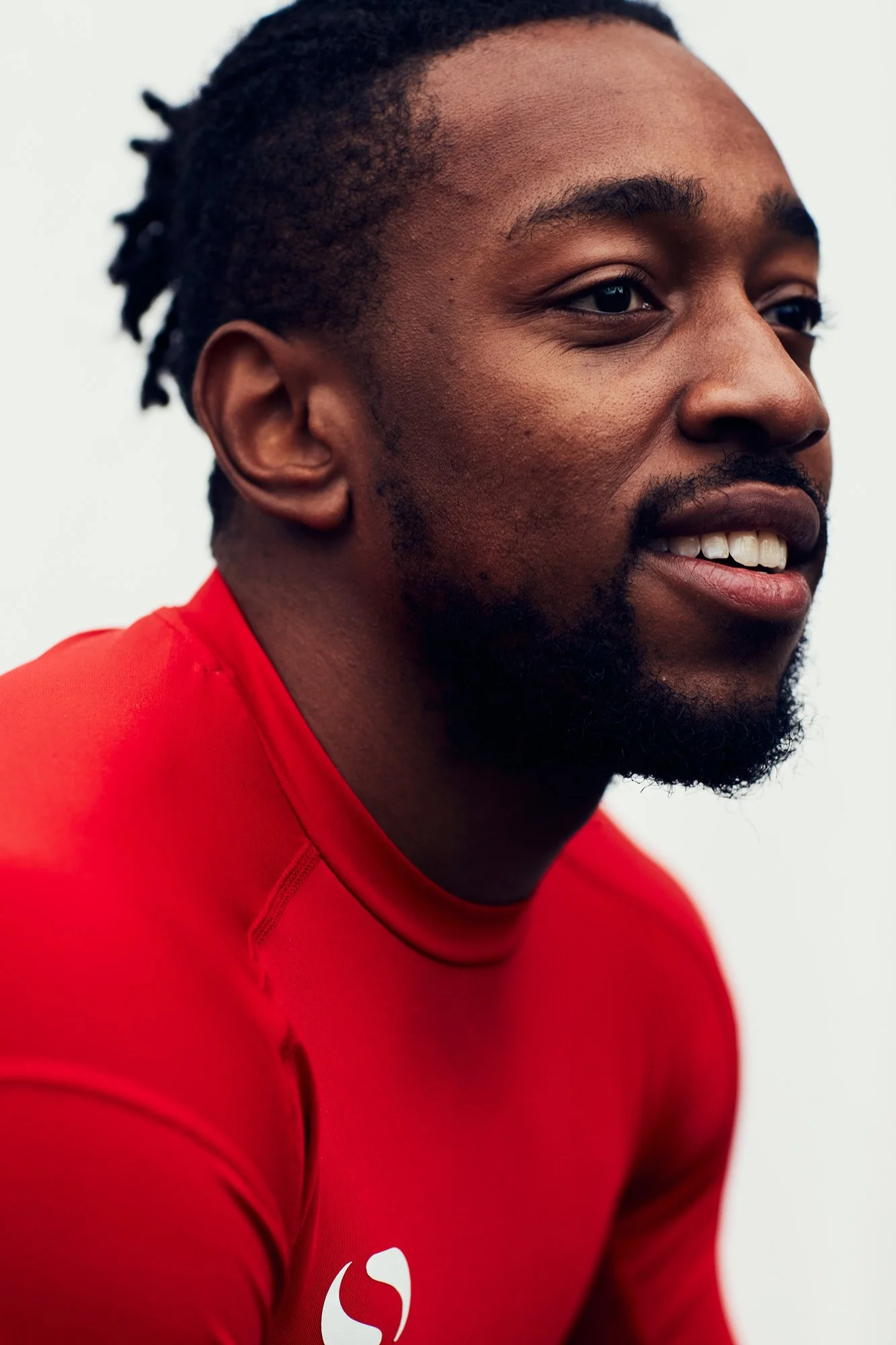 Close-up of a smiling Black man with a beard, wearing a red athletic shirt.