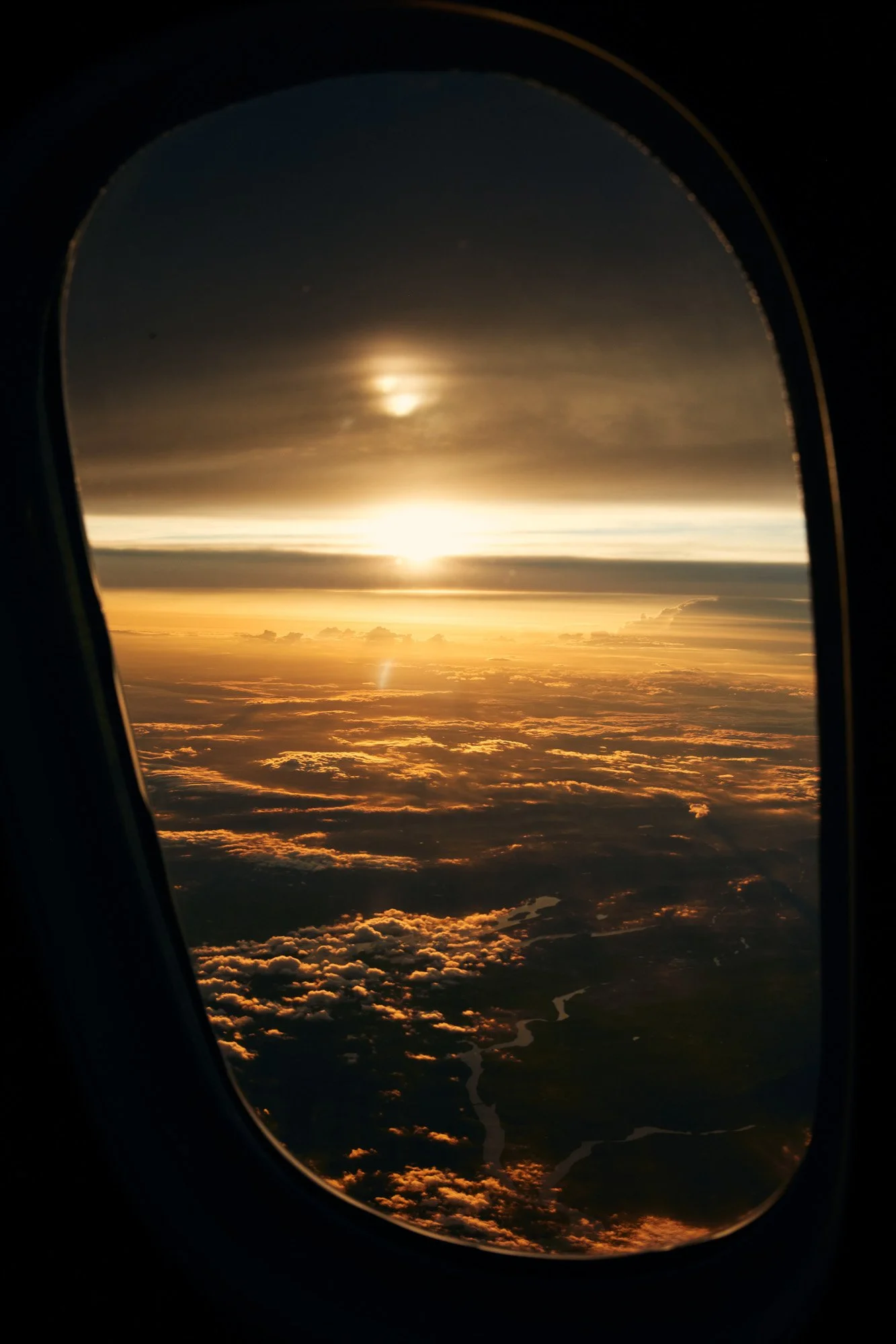 View of a sunset over the clouds and landscape, seen through an airplane window.