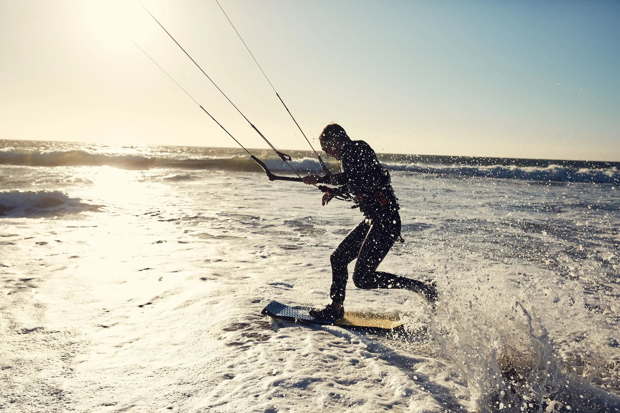 Person kiteboarding on the ocean at sunset at Ocean Beach San Francisco, with waves and spray.