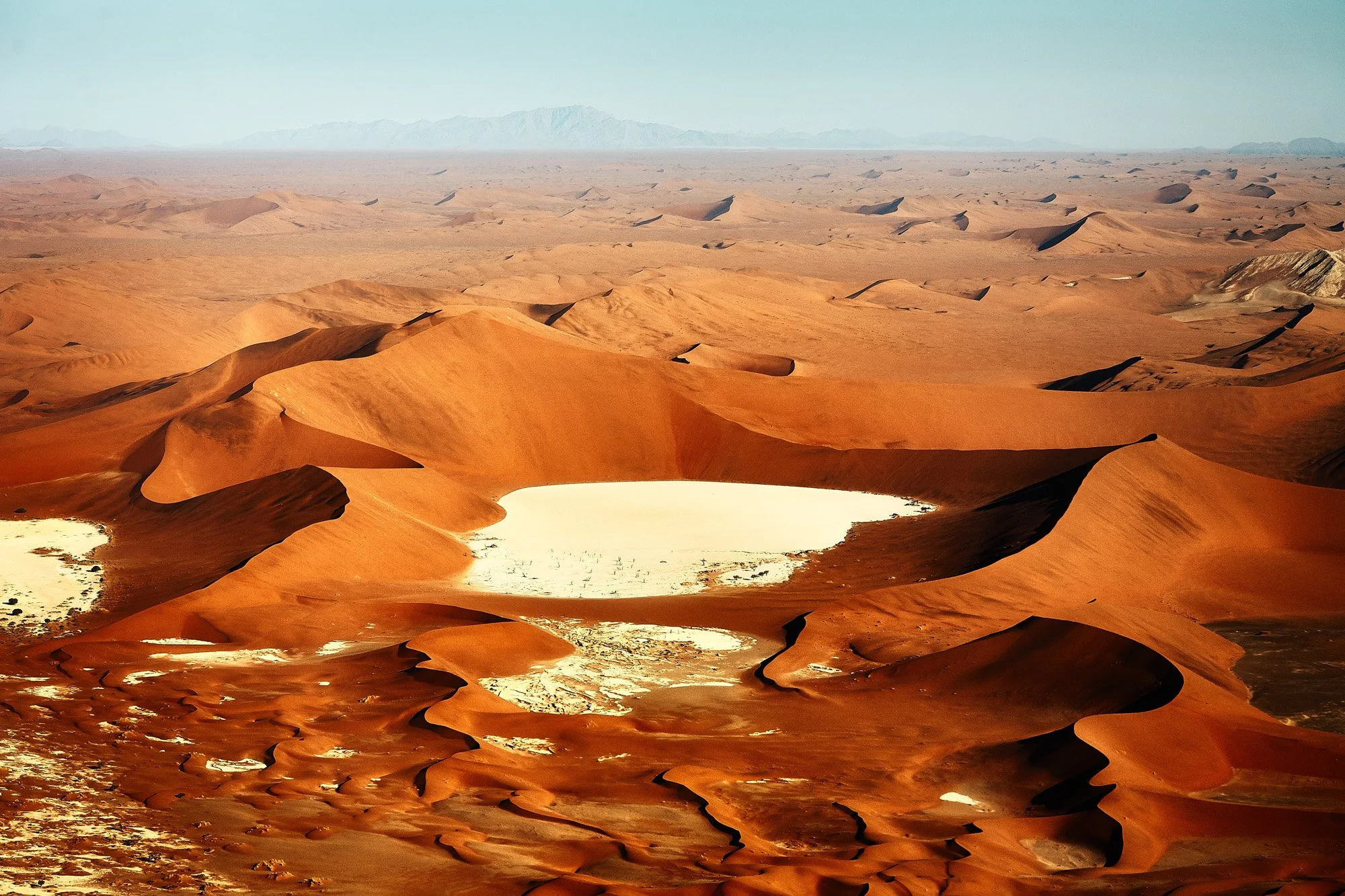 Aerial view of desert landscape Sossusvlei Namib Desert Namibia with sand dunes and two small white salt lakes, distant mountains under a clear sky.