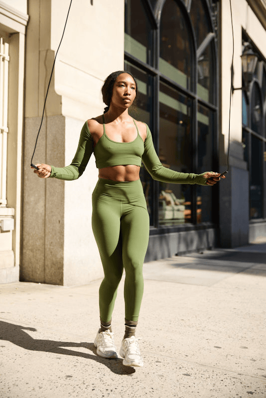 Young Black woman Francia Cooper in green workout outfit jumping rope on New York City sidewalk