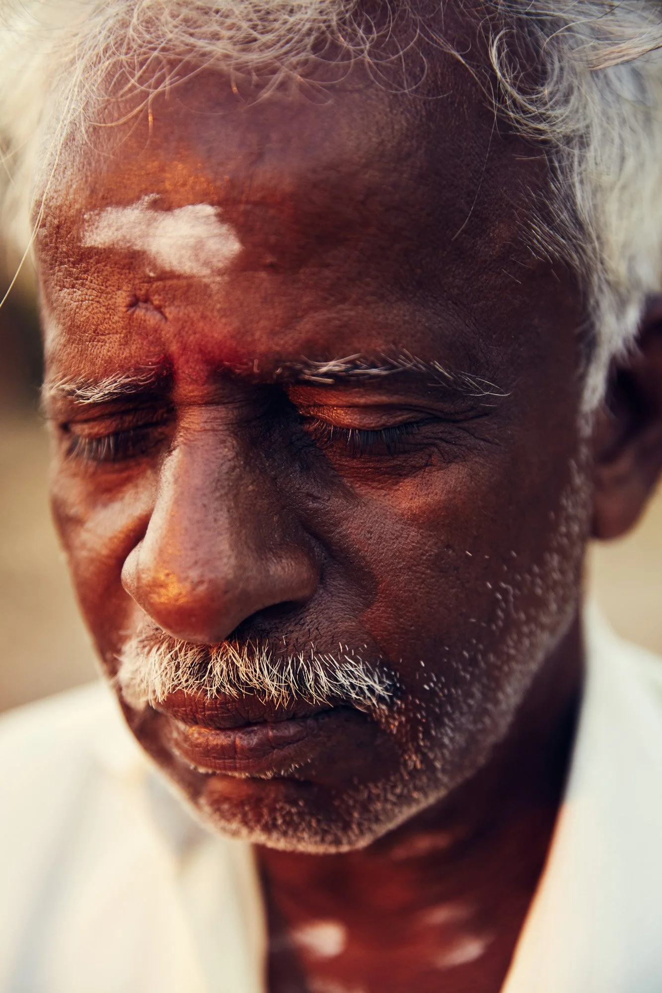 Close-up of an elderly man with dark skin, closed eyes, and gray hair and beard in Jaffna Sri Lanka