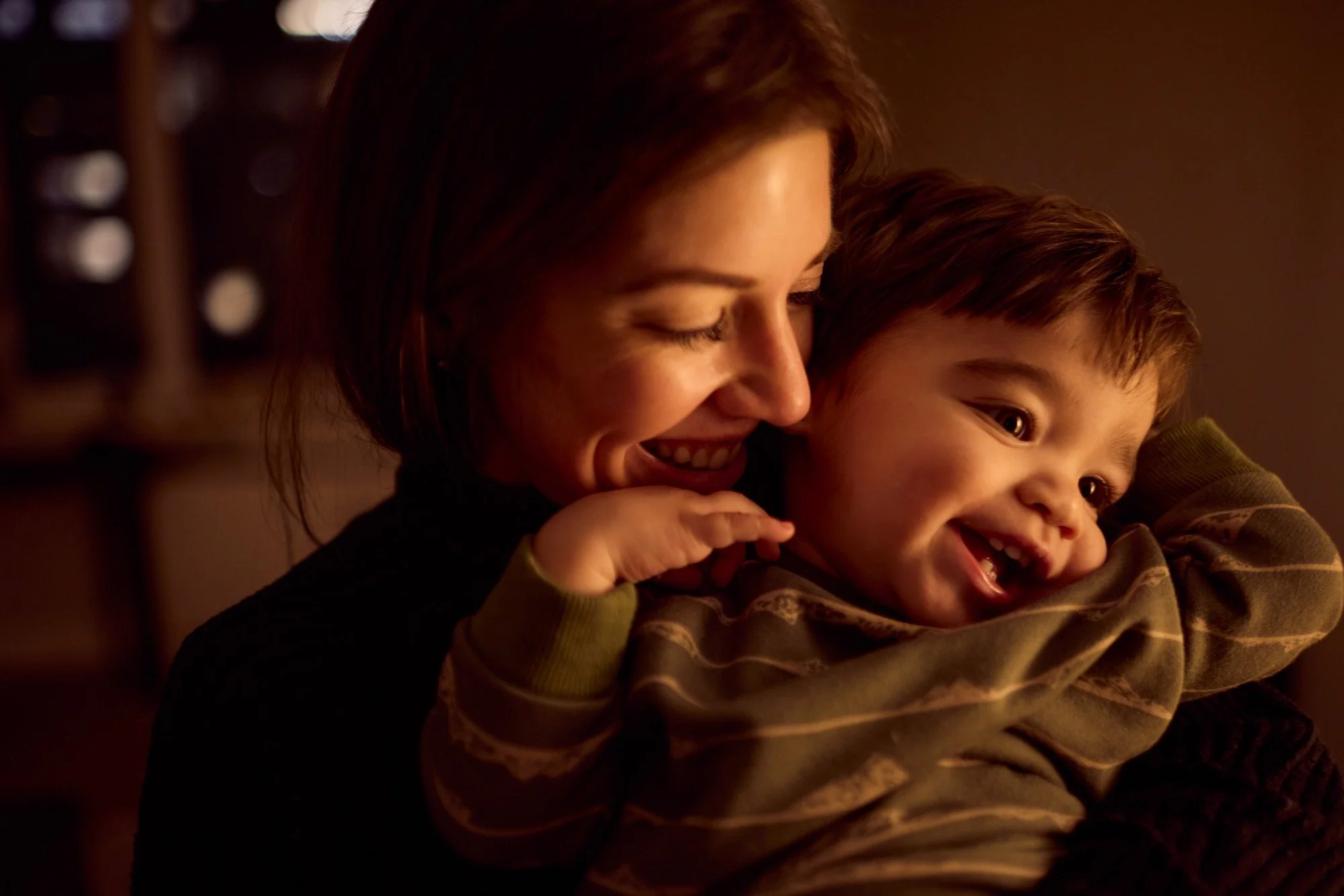 A mother and her little boy sharing a joyful moment indoors, smiling and laughing as they embrace.