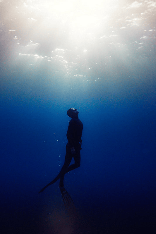 A person underwater wearing a diving mask, with sunlight shining from above, surrounded by deep blue water. Roatan Honduras