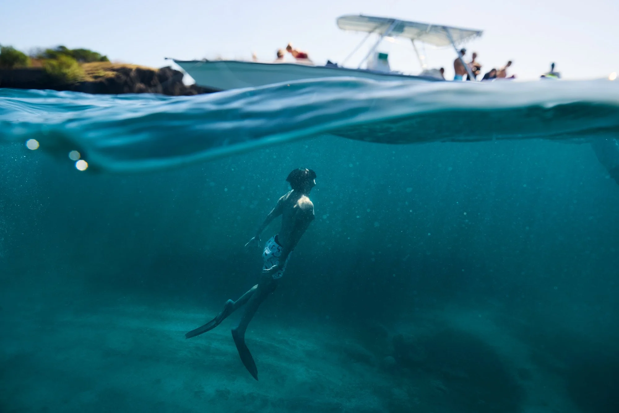 A boy swimming in the ocean with a boat and people on the shore above water in Bequia.