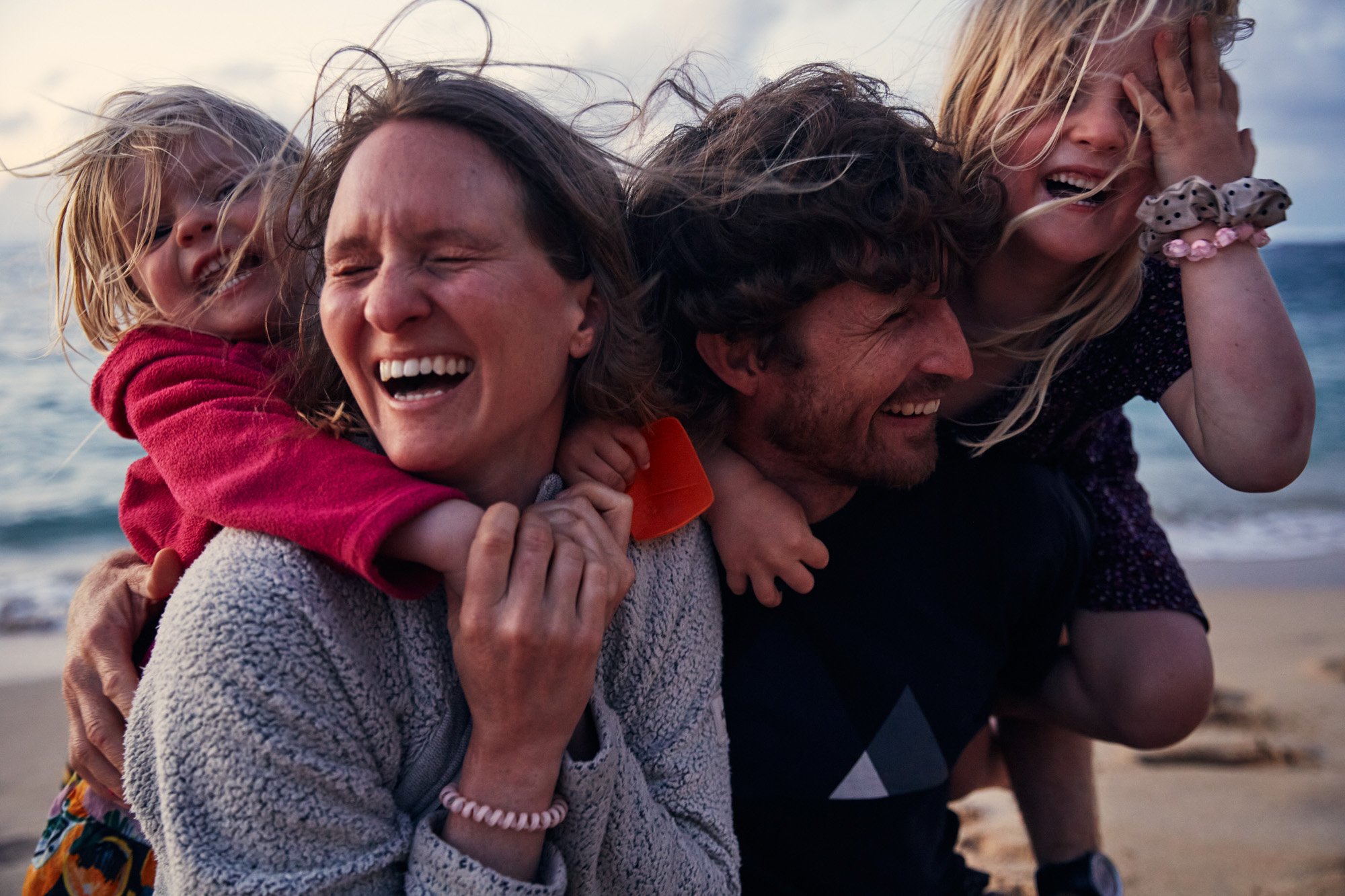 A happy family on the beach, with two children and two adults, all smiling and enjoying a playful moment.