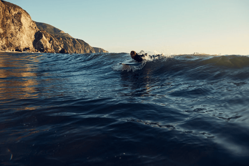 Person surfing on a wave in Big Sur on a rocky coastline during sunset.