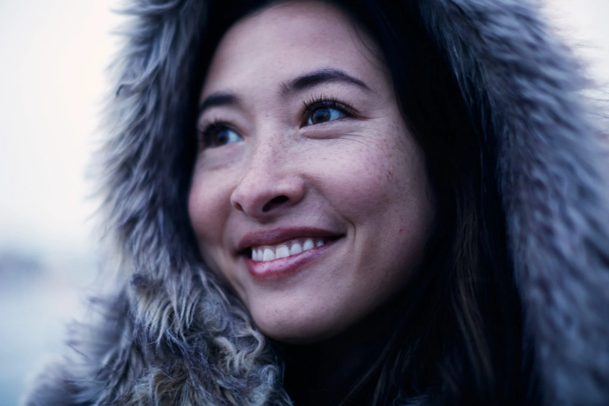Close-up of a smiling woman, wearing a thick, faux fur hooded coat.