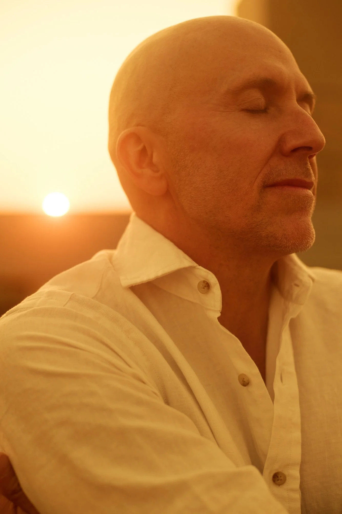 Lee Burridge with closed eyes, wearing a white shirt, sitting calmly during sunset in New York City