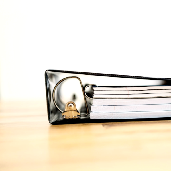 Close-up of a black binder clip holding a stack of white papers on a wooden surface.
