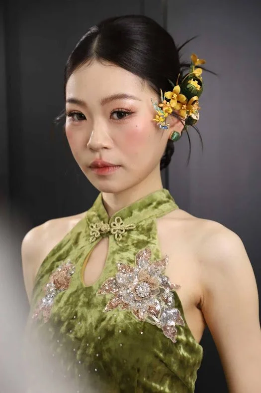 Bride dressed in a traditional Chinese qipao with floral embroidery, smiling softly, with her hair styled in an elegant updo with floral and tassel hair accessories. Make up by make up artist Muacher (Cheron Tan)