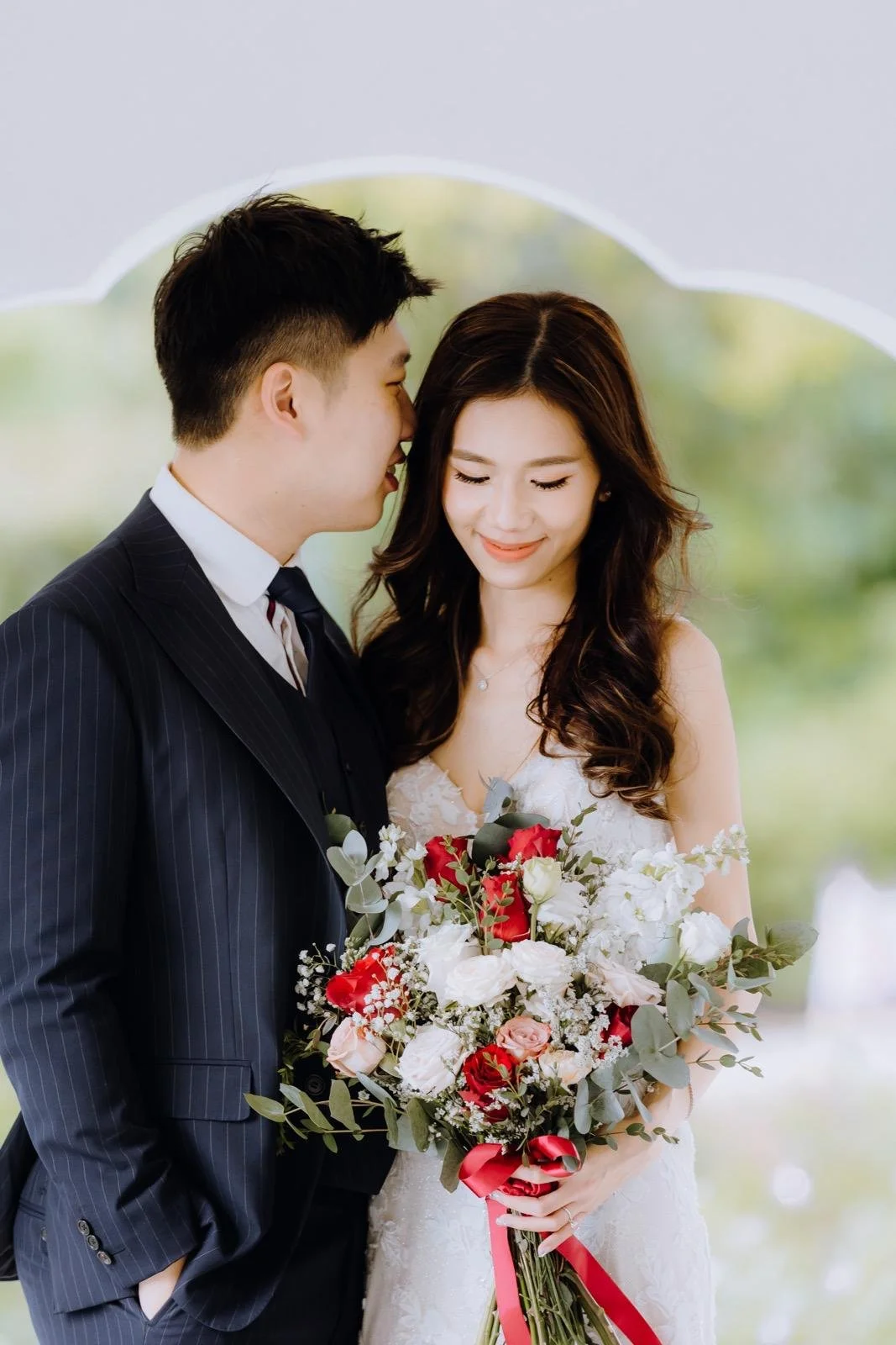 A smiling bride holding beautiful hand bouquet and groom standing in a beautiful pavilion. Make up by make up artist Muacher (Cheron Tan)