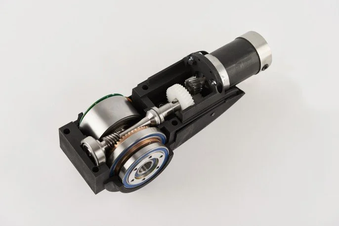 Close-up of a small electric motor with gears and mechanical components mounted on a black base.