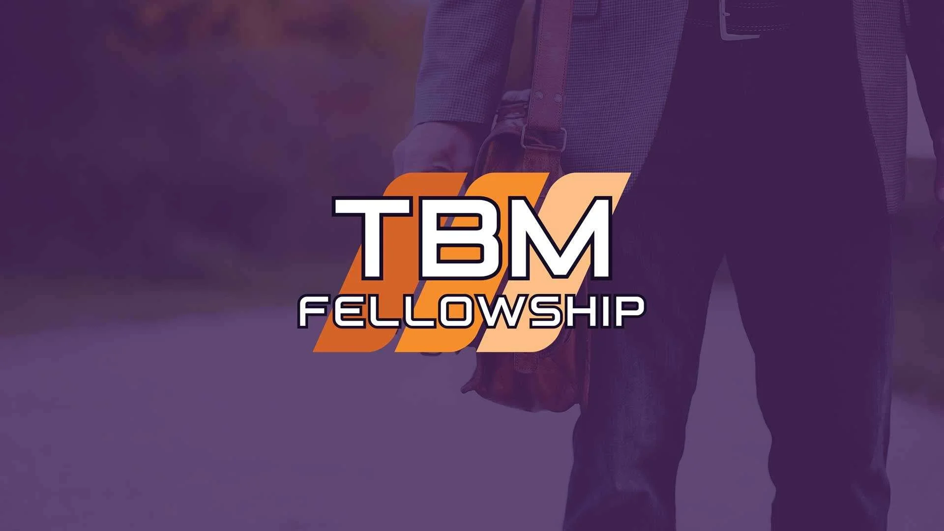 Logo for TBM Fellowship with stylized orange and beige letters 'TBM' and the word 'Fellowship' underneath, with a blurred person carrying a bag in the background.