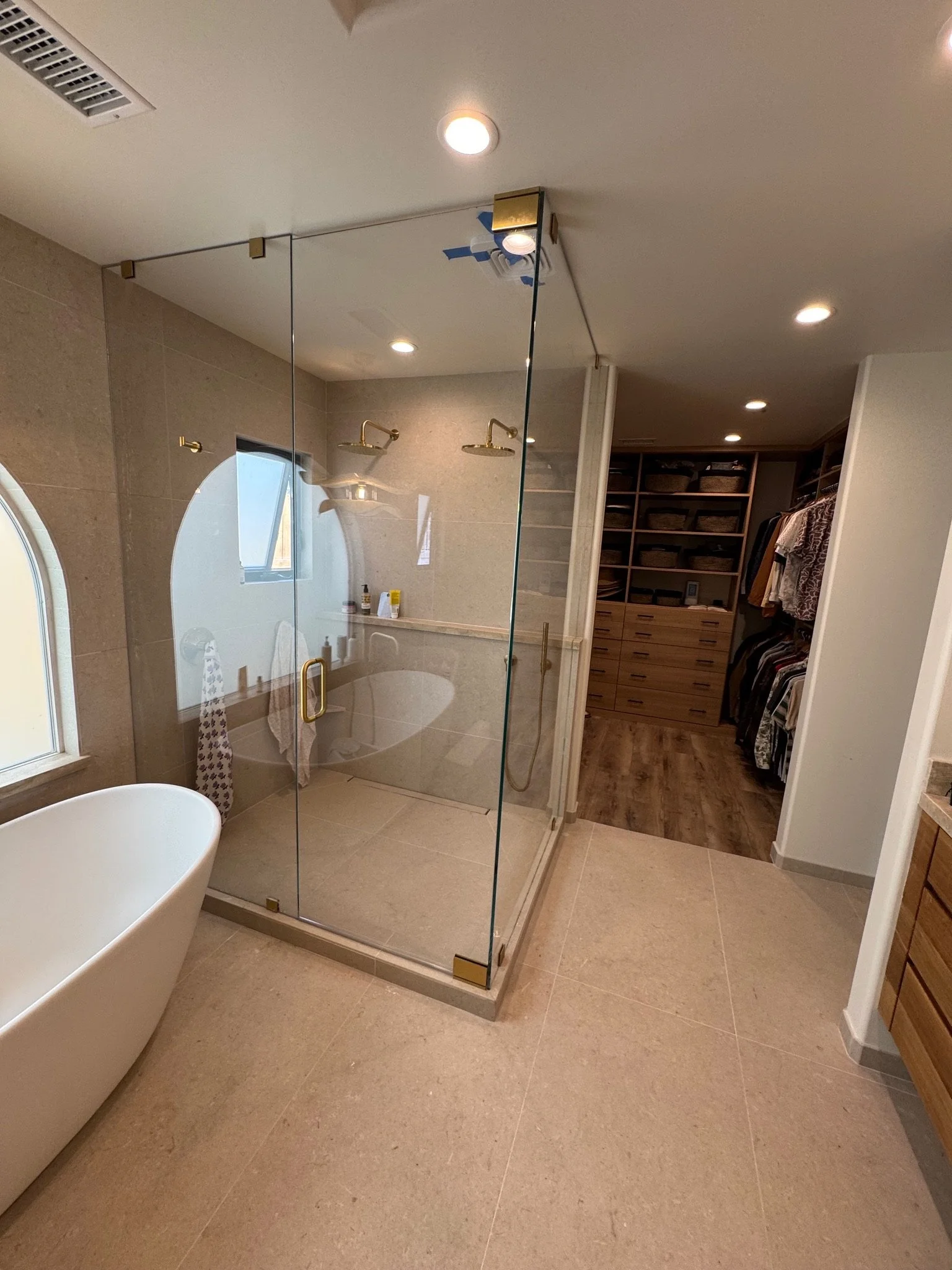 Modern bathroom with walk-in glass shower, freestanding bathtub, wooden cabinetry, and walk-in closet with open shelves and clothing.