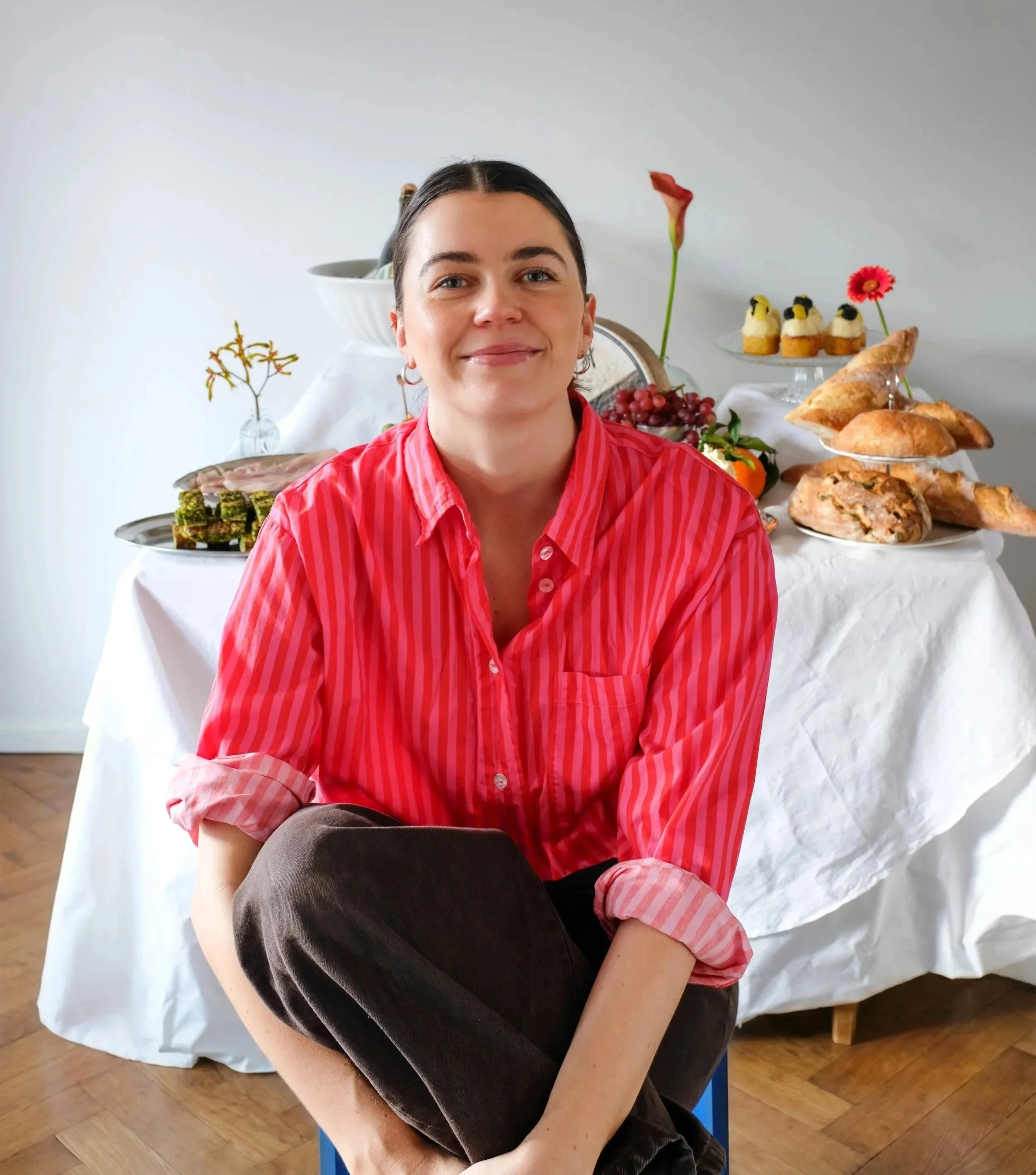 Larissa Sterchi in red and pink striped shirt sitting in front of a table with food and desserts.