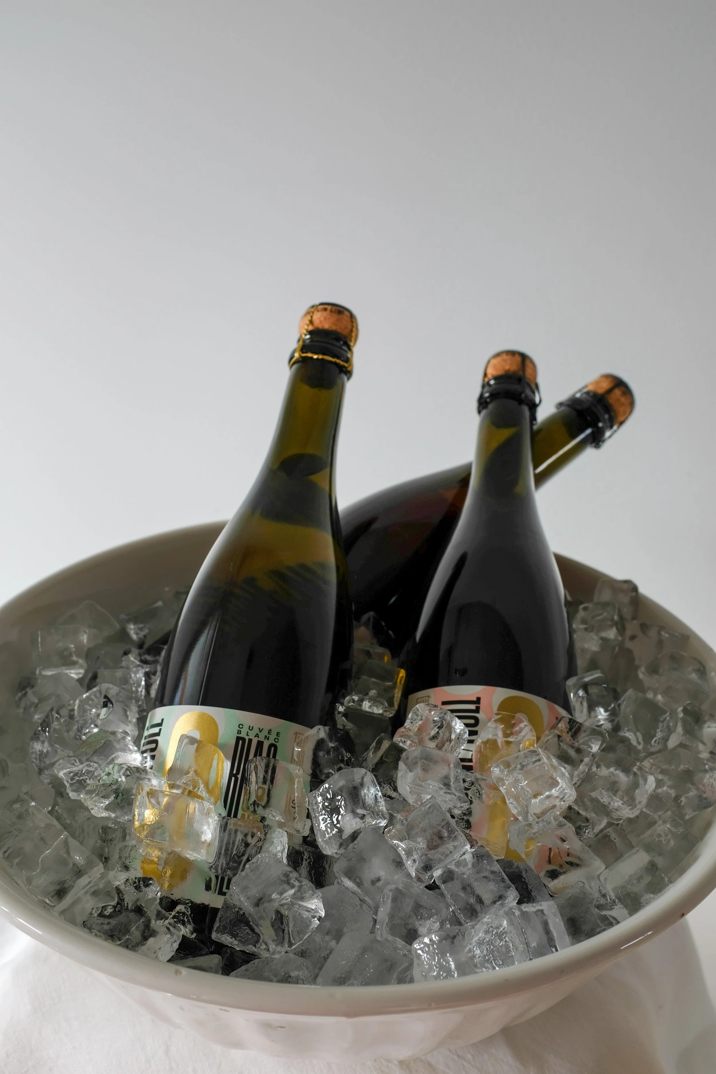 Three bottles of sparkling wine chilling in a bowl of ice cubes.
