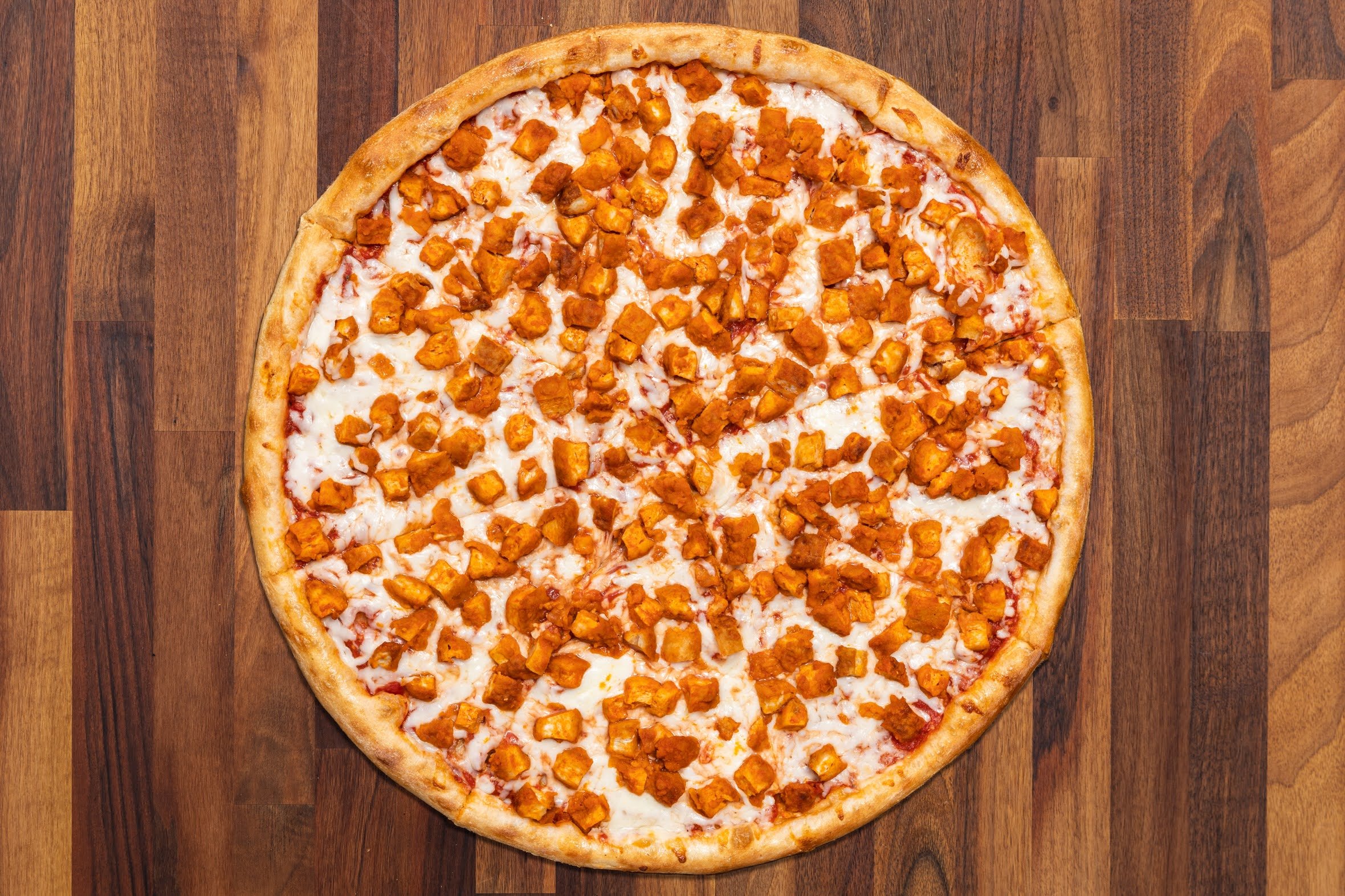 A whole pizza topped with buffalo chicken pieces and melted cheese on a wooden surface.