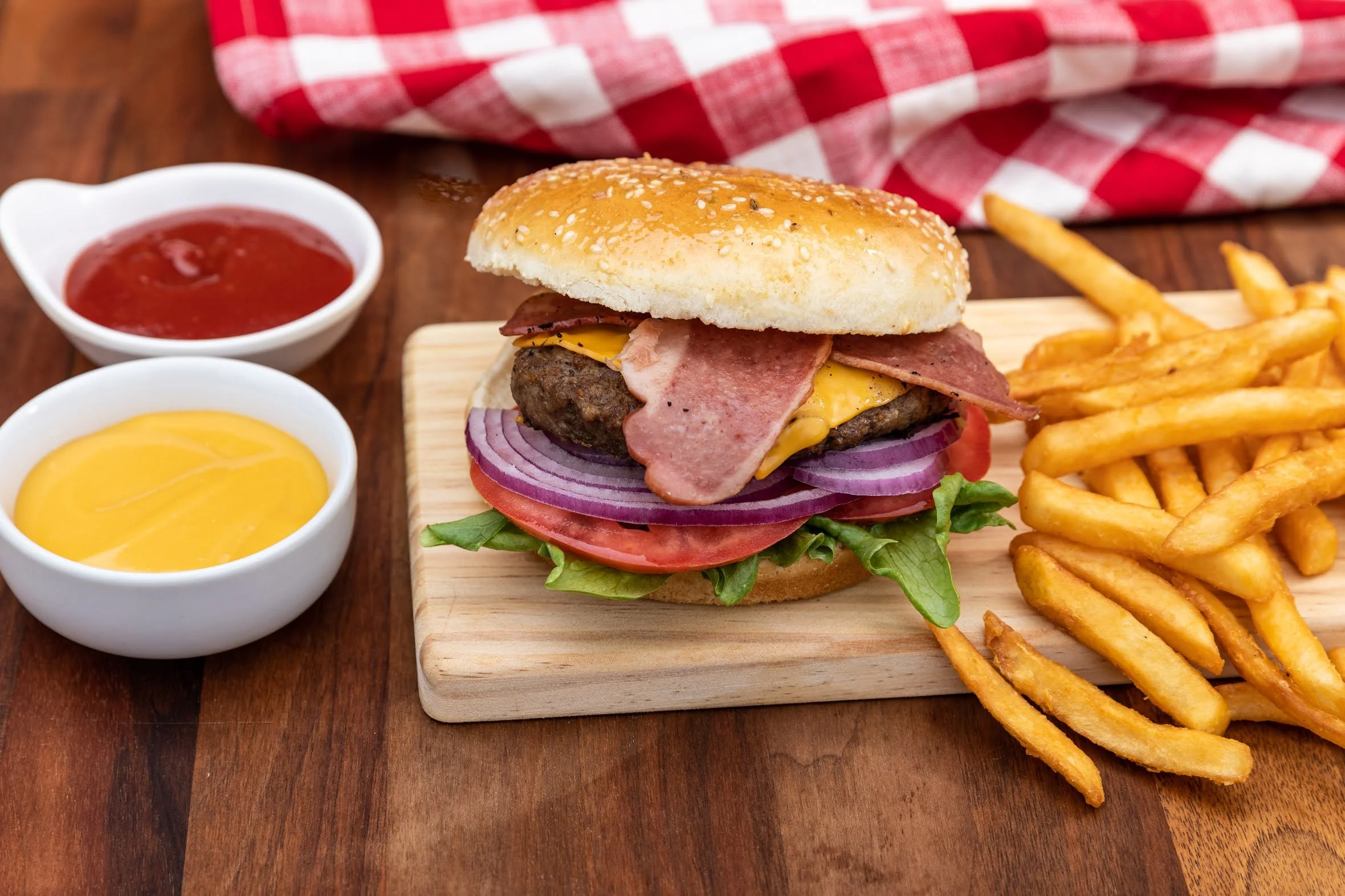 Hamburger with French fries, ketchup, and mustard on a wooden table.