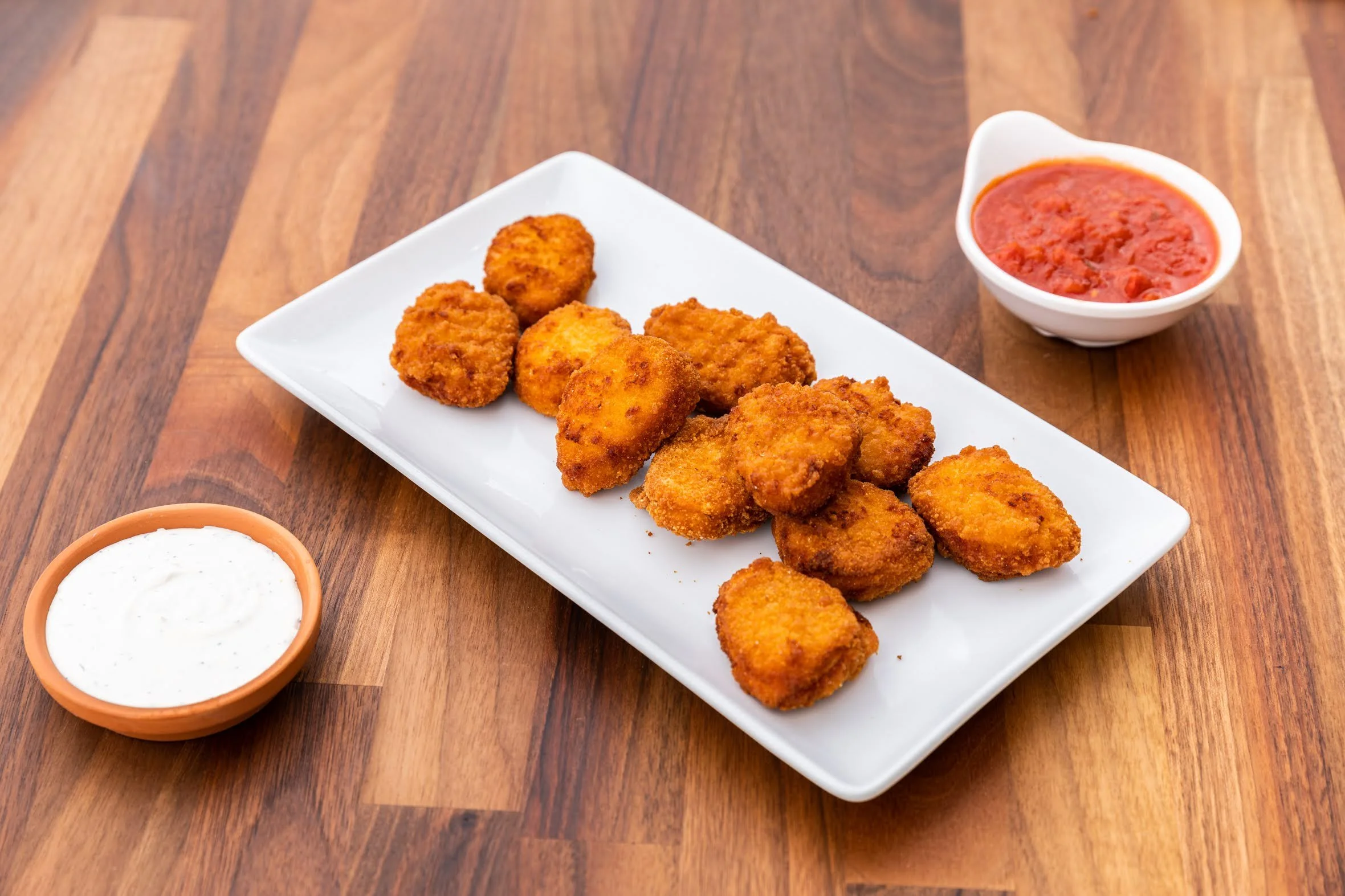 Fried chicken nuggets with three bowls of dipping sauces on a wooden table.