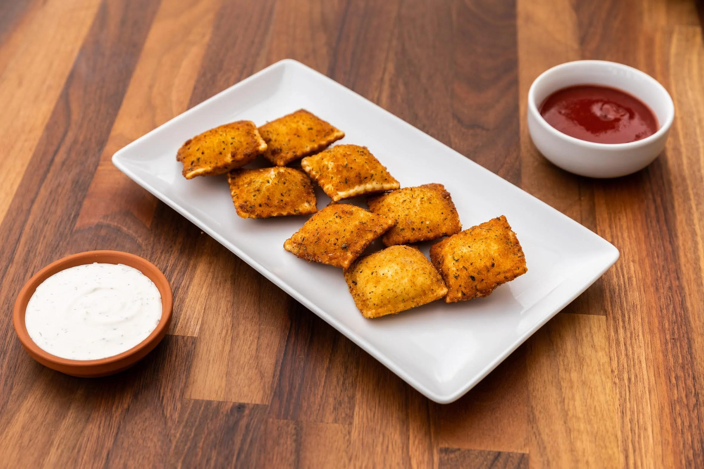 Plate of fried fish fillets with two bowls of dipping sauces, one with red sauce and the other with white sauce, on a wooden table.