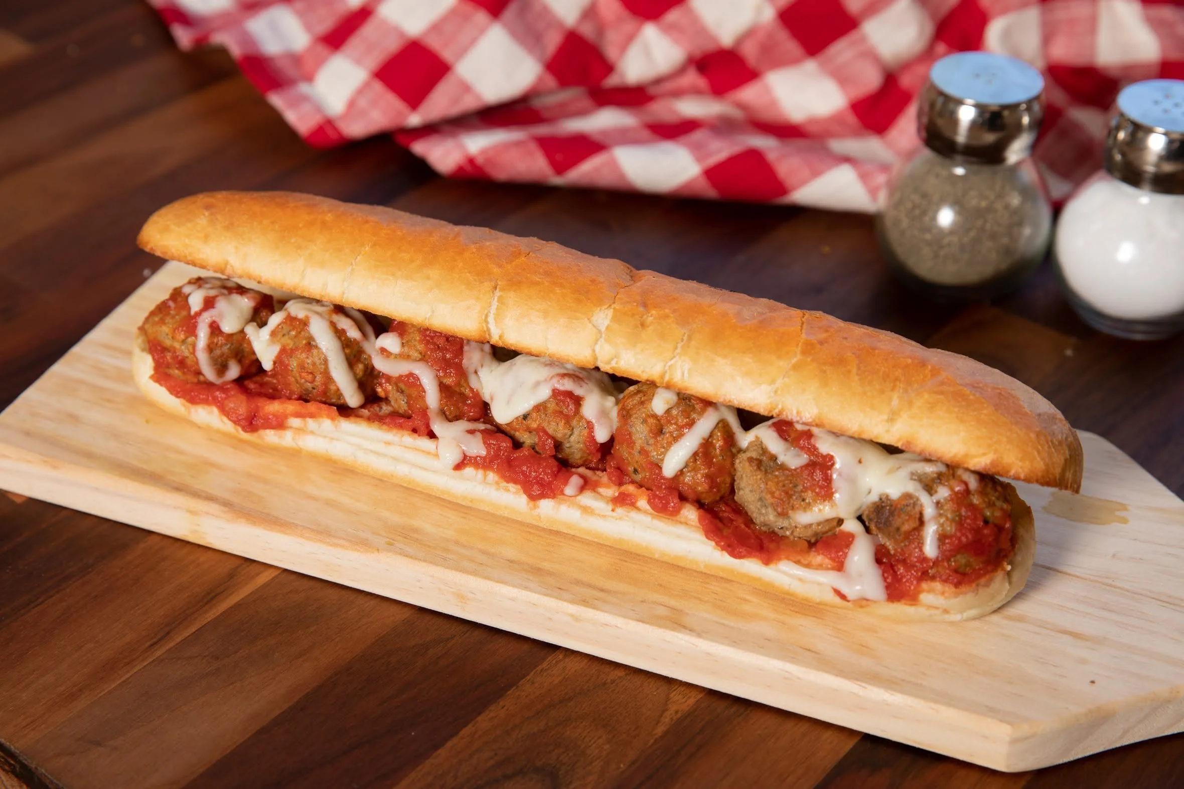 Italian meatball sub sandwich with meatballs, marinara sauce, and melted cheese on a hoagie bun sitting on a wooden cutting board.