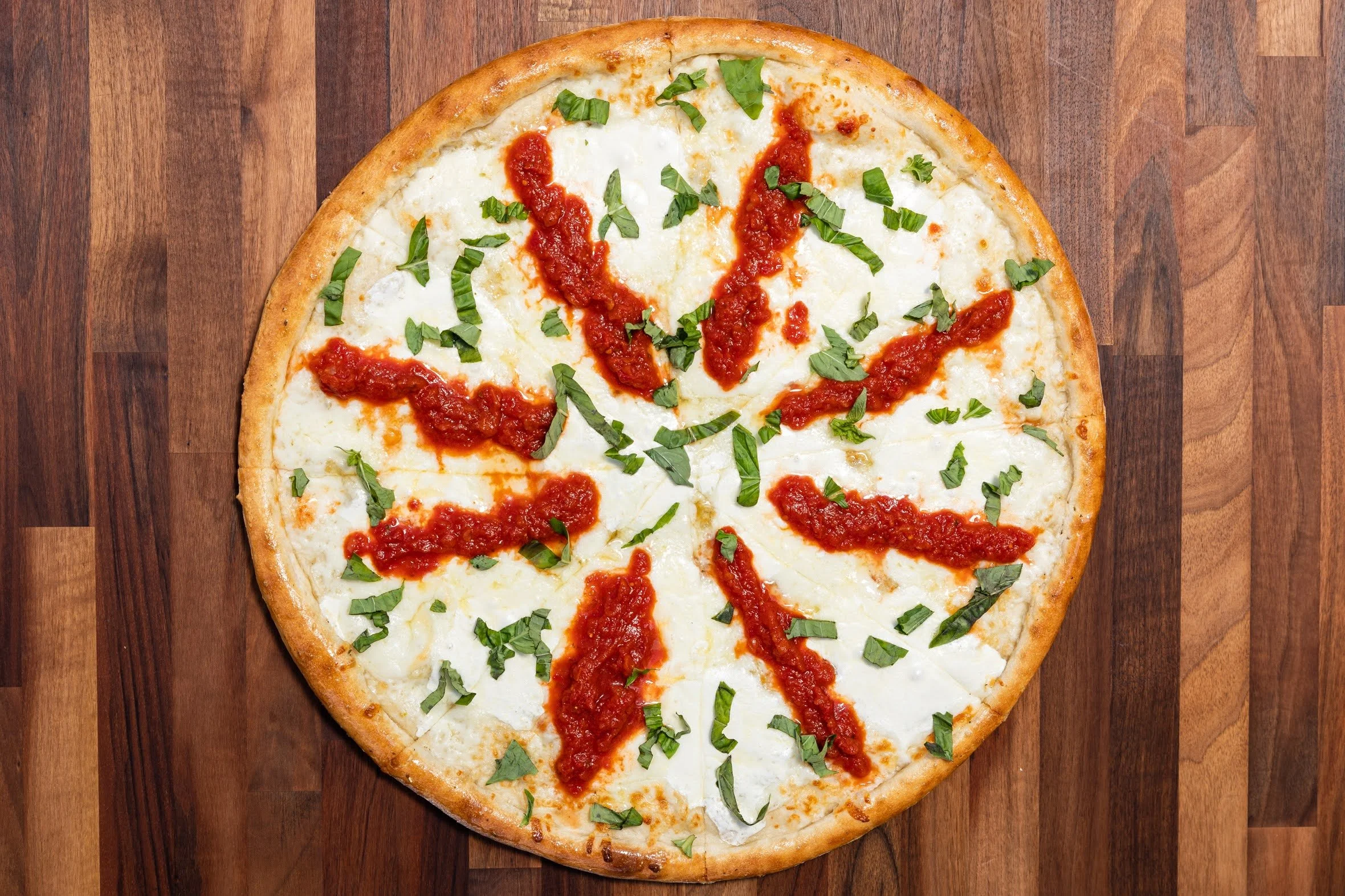 Round pizza with cheese, tomato sauce, and chopped basil on a wooden surface.