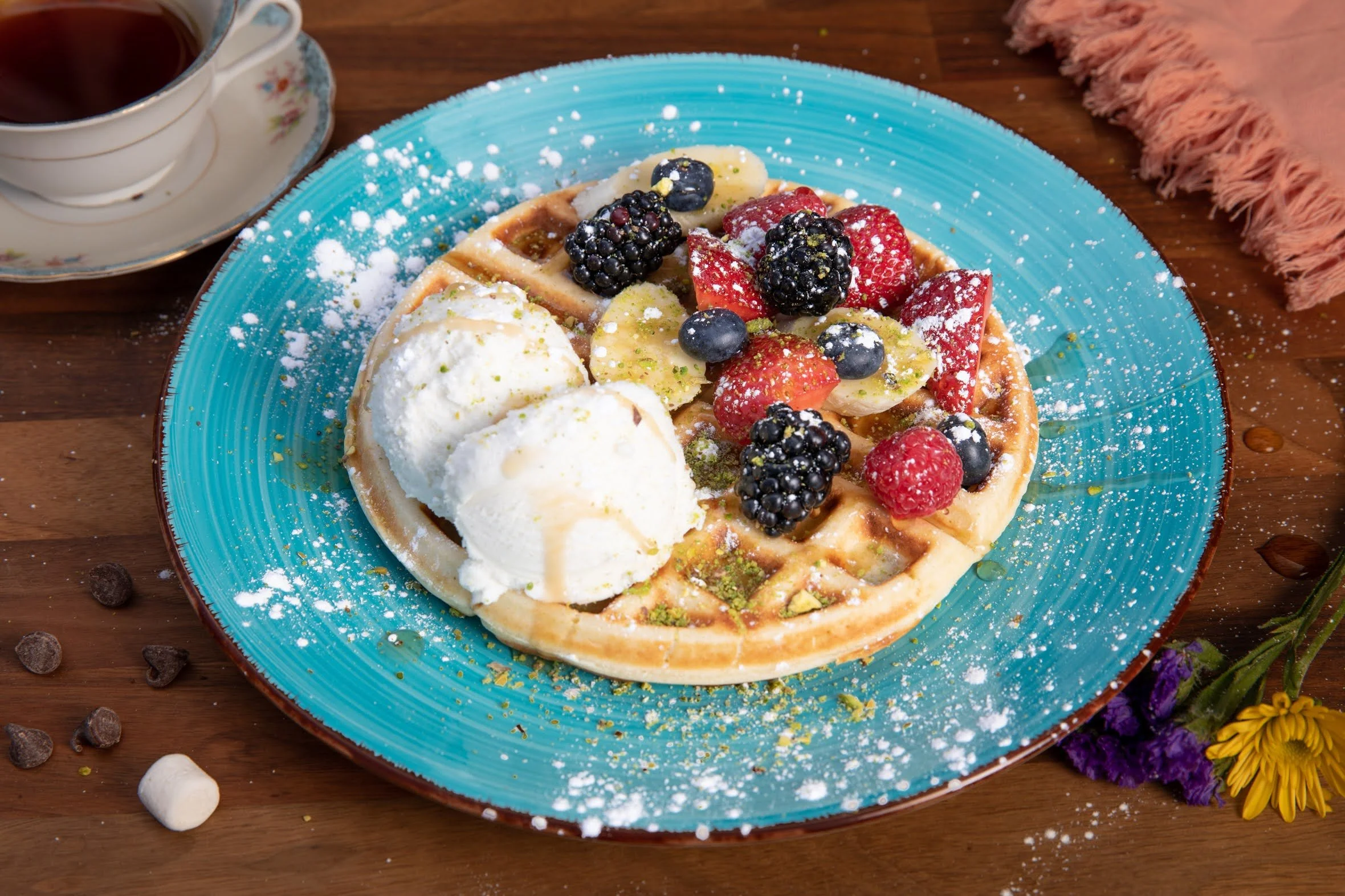 A plate of waffles topped with mixed berries, a scoop of vanilla ice cream, and drizzled with syrup, served on a bright blue plate.