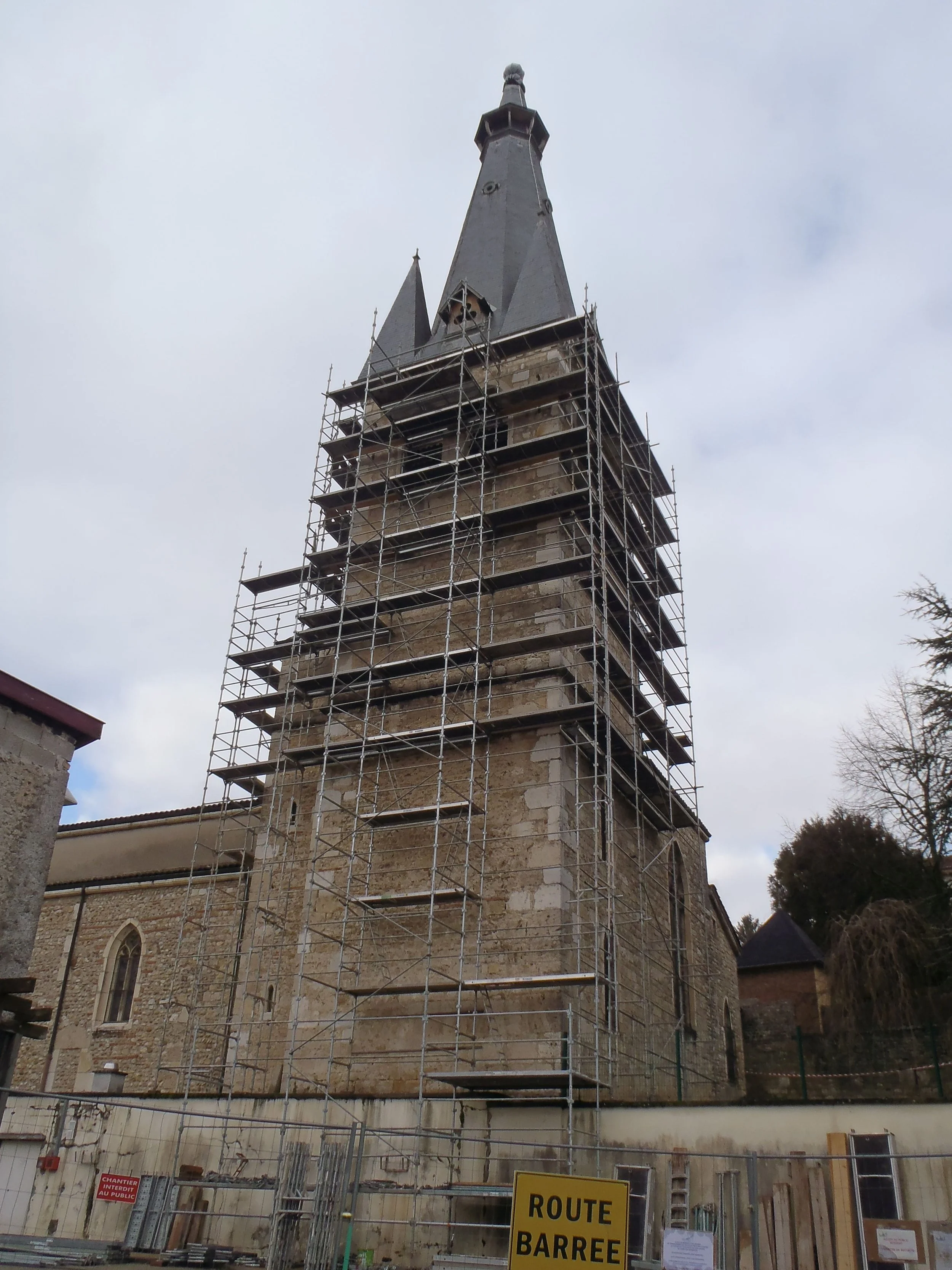 Une grue entoure une tour d'une vieille église sous restauration, avec un ciel nuageux en arrière-plan.