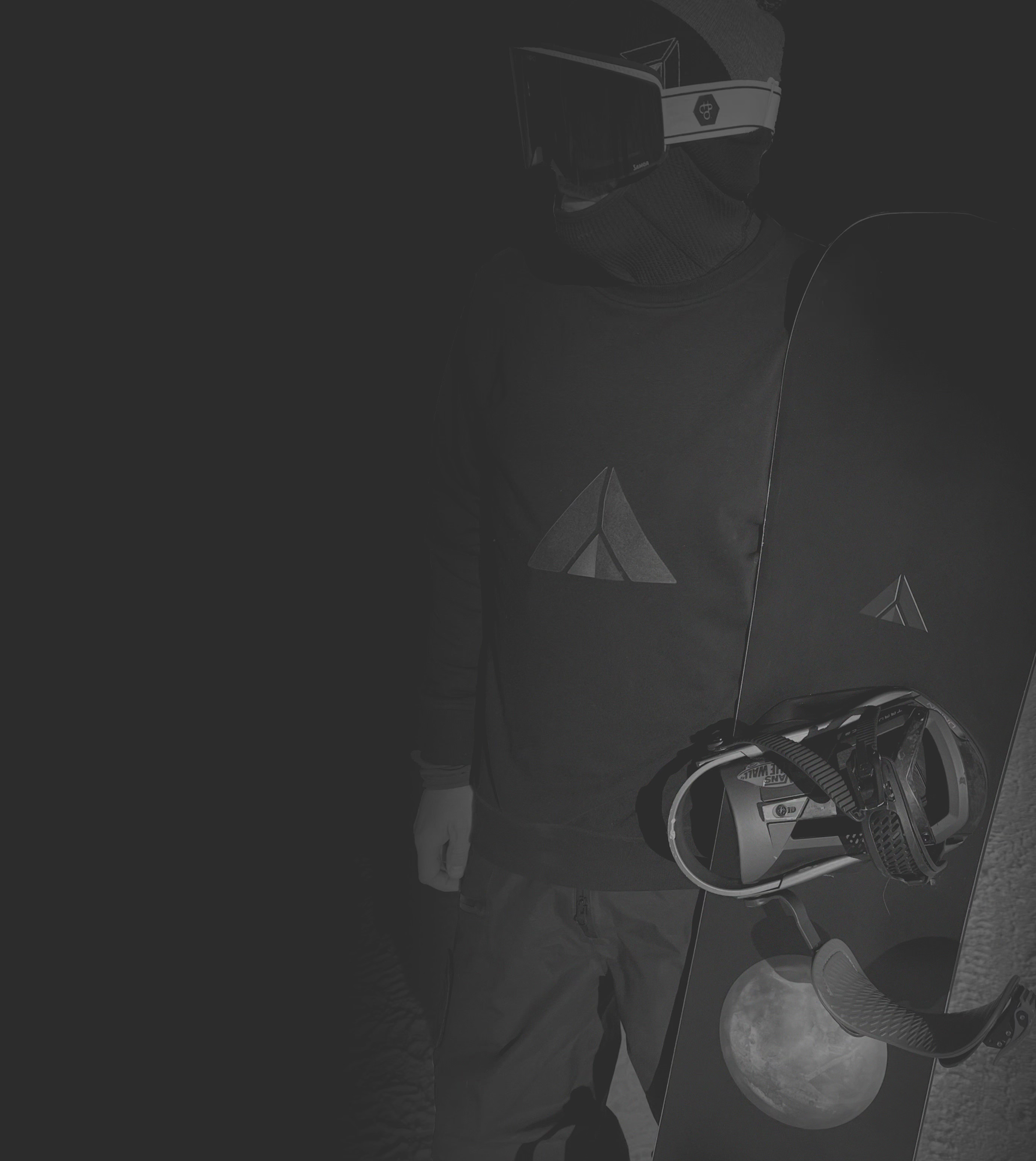 A person wearing a virtual reality headset and holding a snowboard with a moon and mountain design, standing against a dark background.