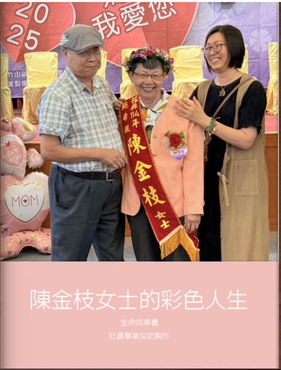 Three women standing together at a celebration event. One woman in the middle wears a sash and a flower crown, holding a pink blazer with a corsage. The woman on the right is smiling and has her hands on the blazer. The woman on the left wears glasses and a cap. The background shows a red heart with Chinese characters and balloons, including heart-shaped balloons that say "Love You" and "MOM."