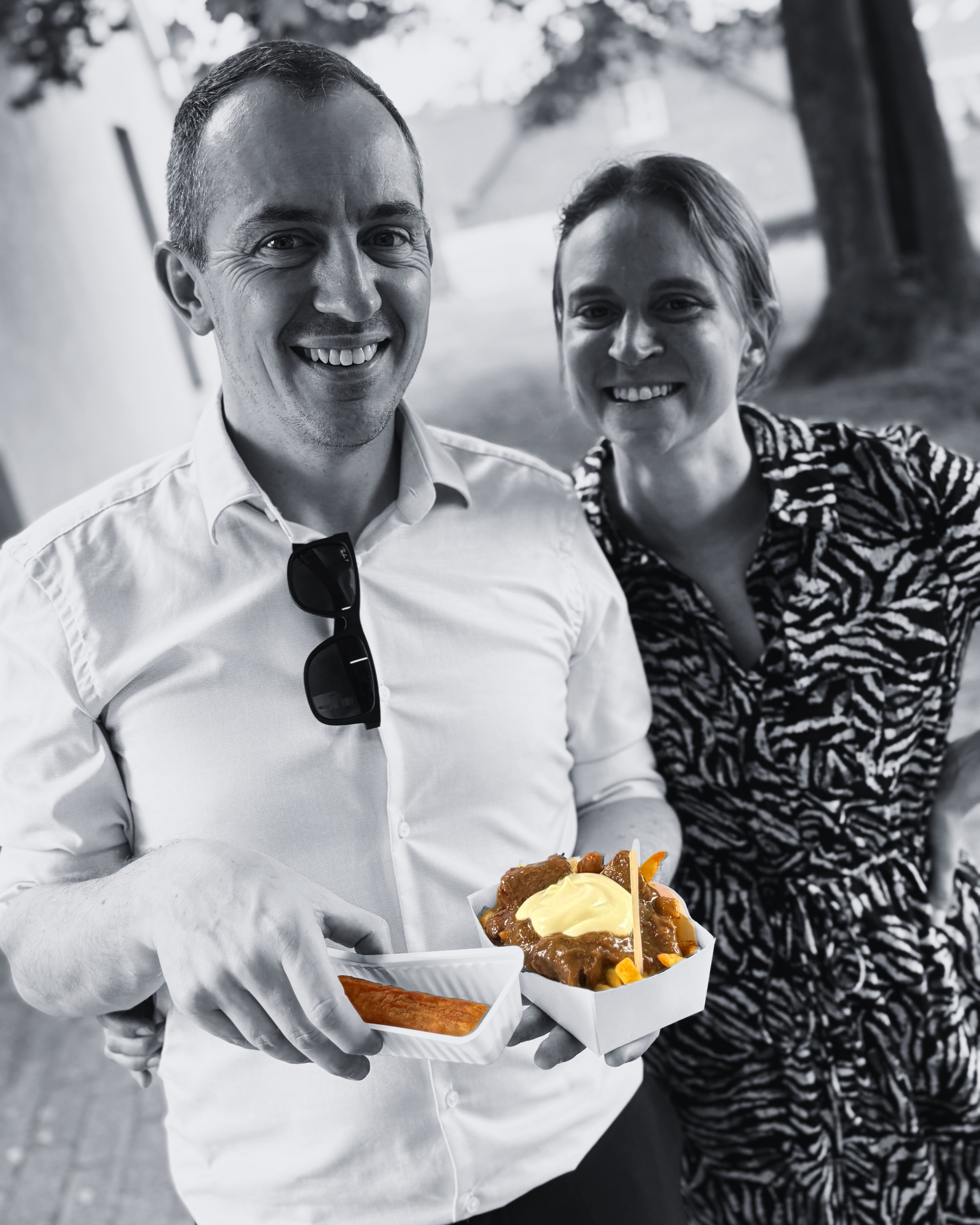 Twee mensen glimlachen en houden snacks en saus, terwijl ze buiten staan.