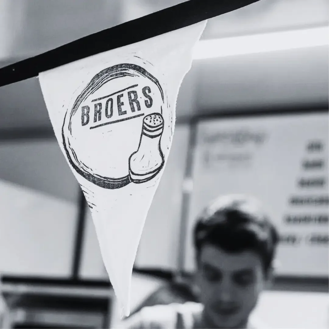 Black and white photo of a paper flag with the logo 'Broers' and an illustration of a salt shaker, hanging inside a store.