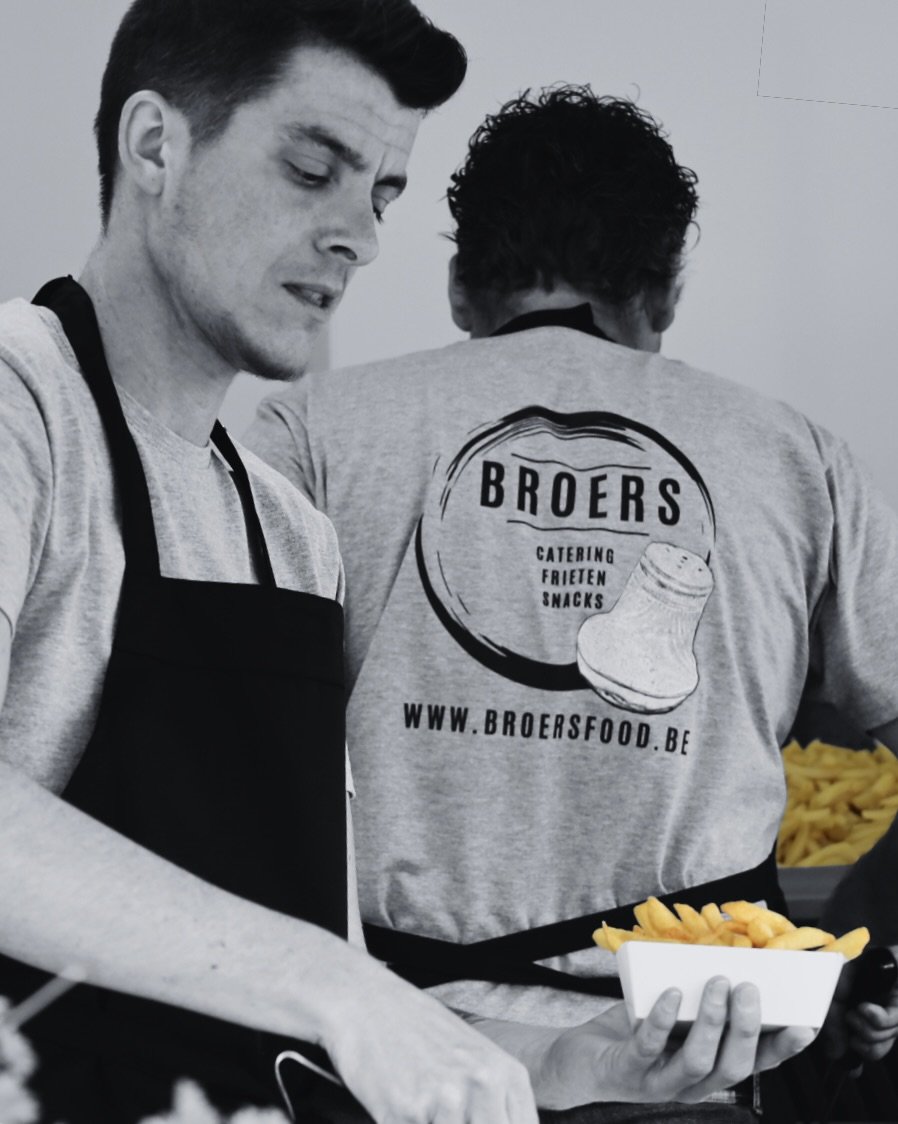 Twee mannen werken bij een foodservice, een van hen houdt een bak frieten.