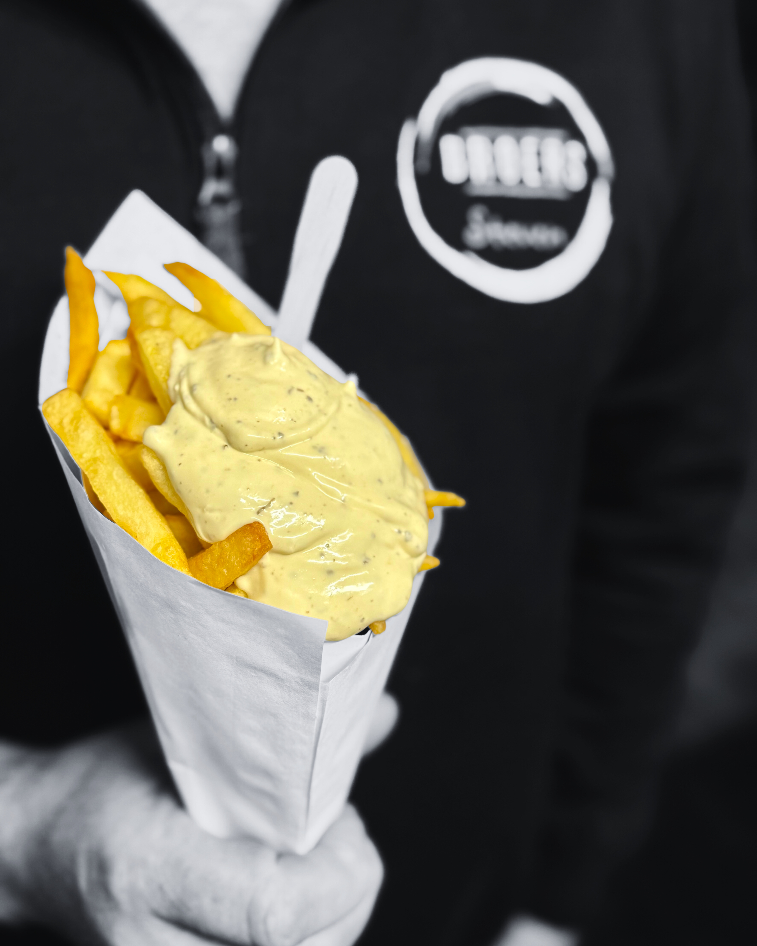 Persoon houdt een portie friet met saus in een papiervrije bak, kleding met een logo in de buurt van de borst.