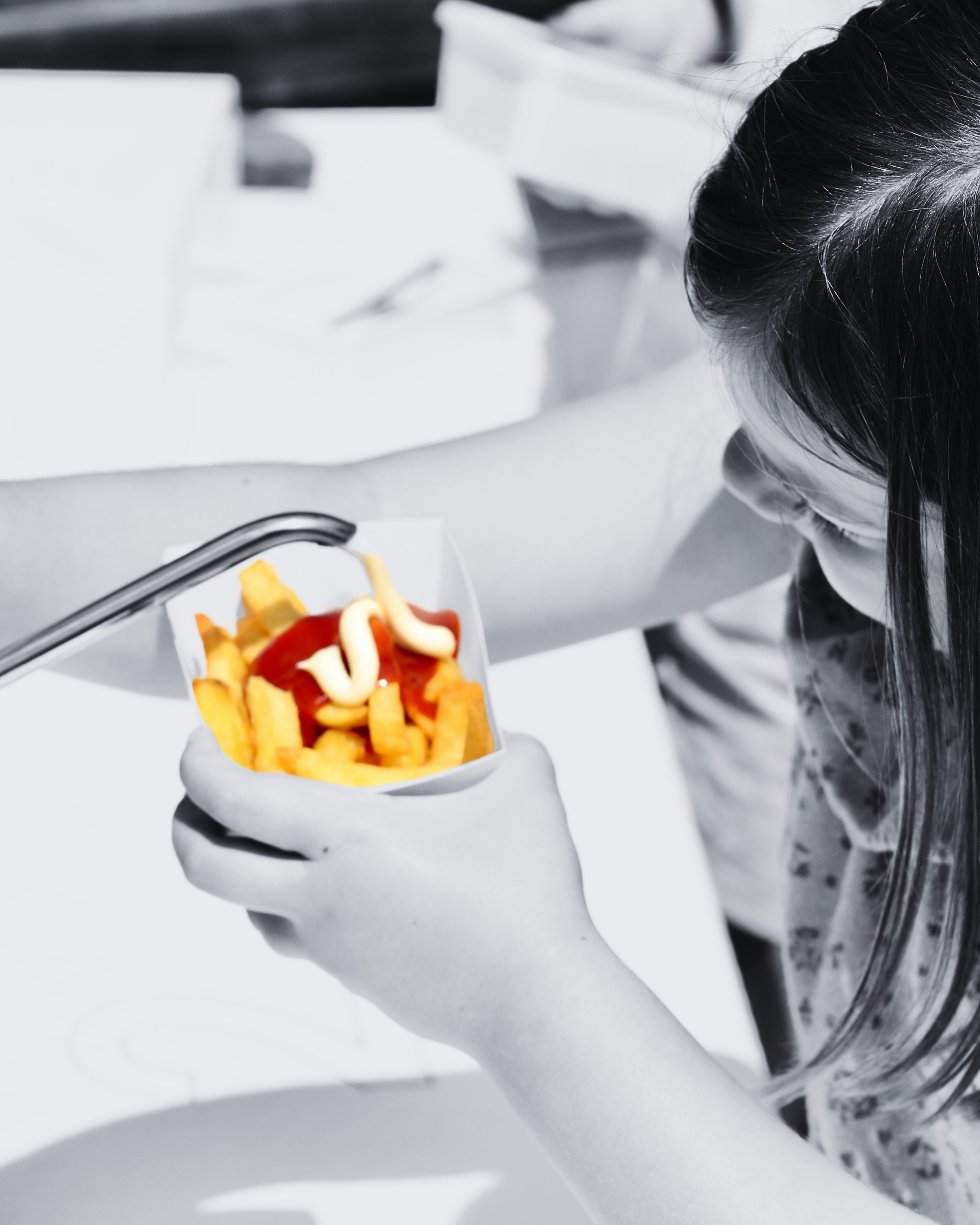 Kleine meisje houdt een bordje met patat en ketchup, met mayonaise erop, in haar hand.