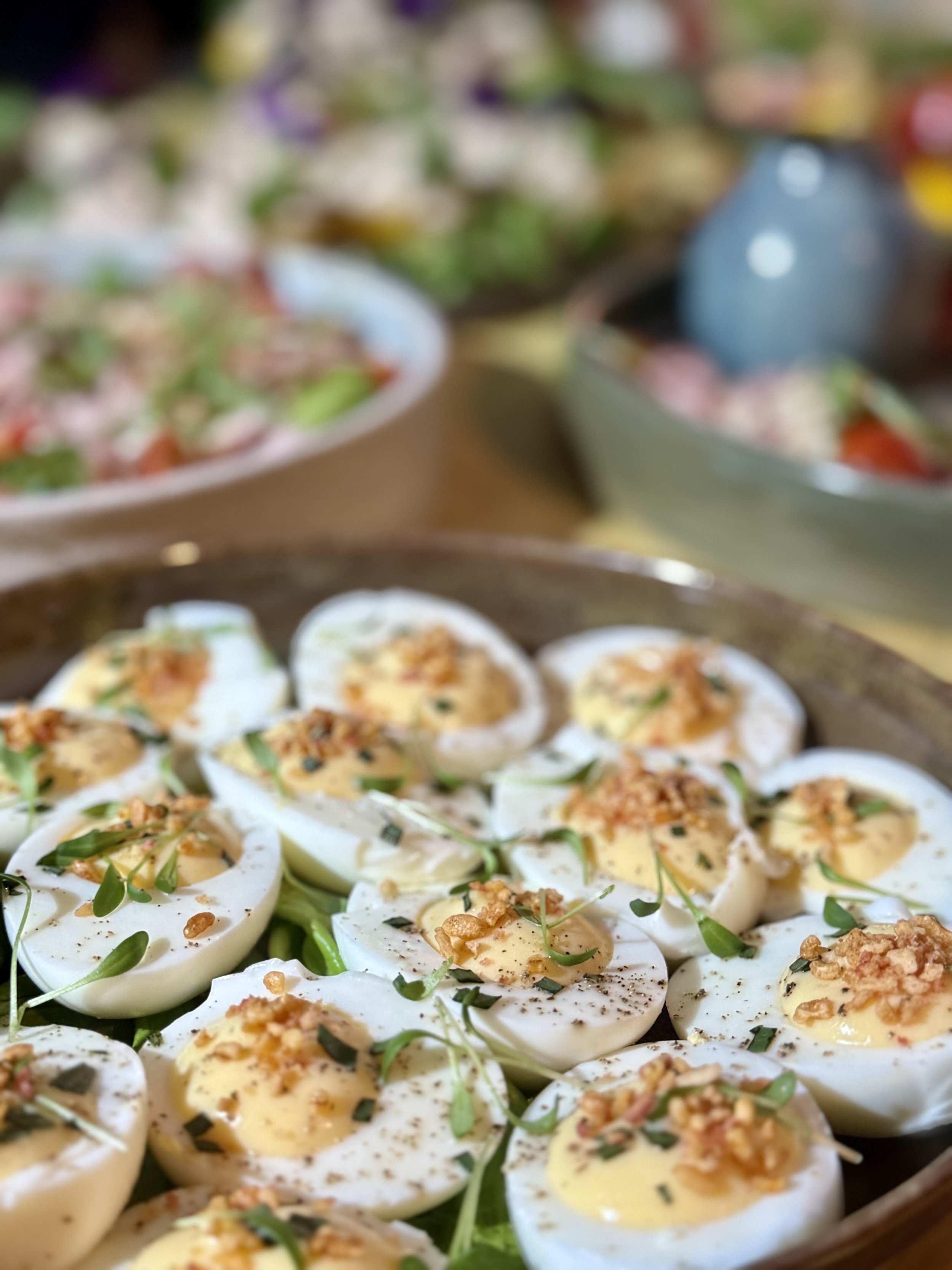 Gevulde eieren met kruiding en greens op een grote schaal, met salade en andere gerechten op de achtergrond.