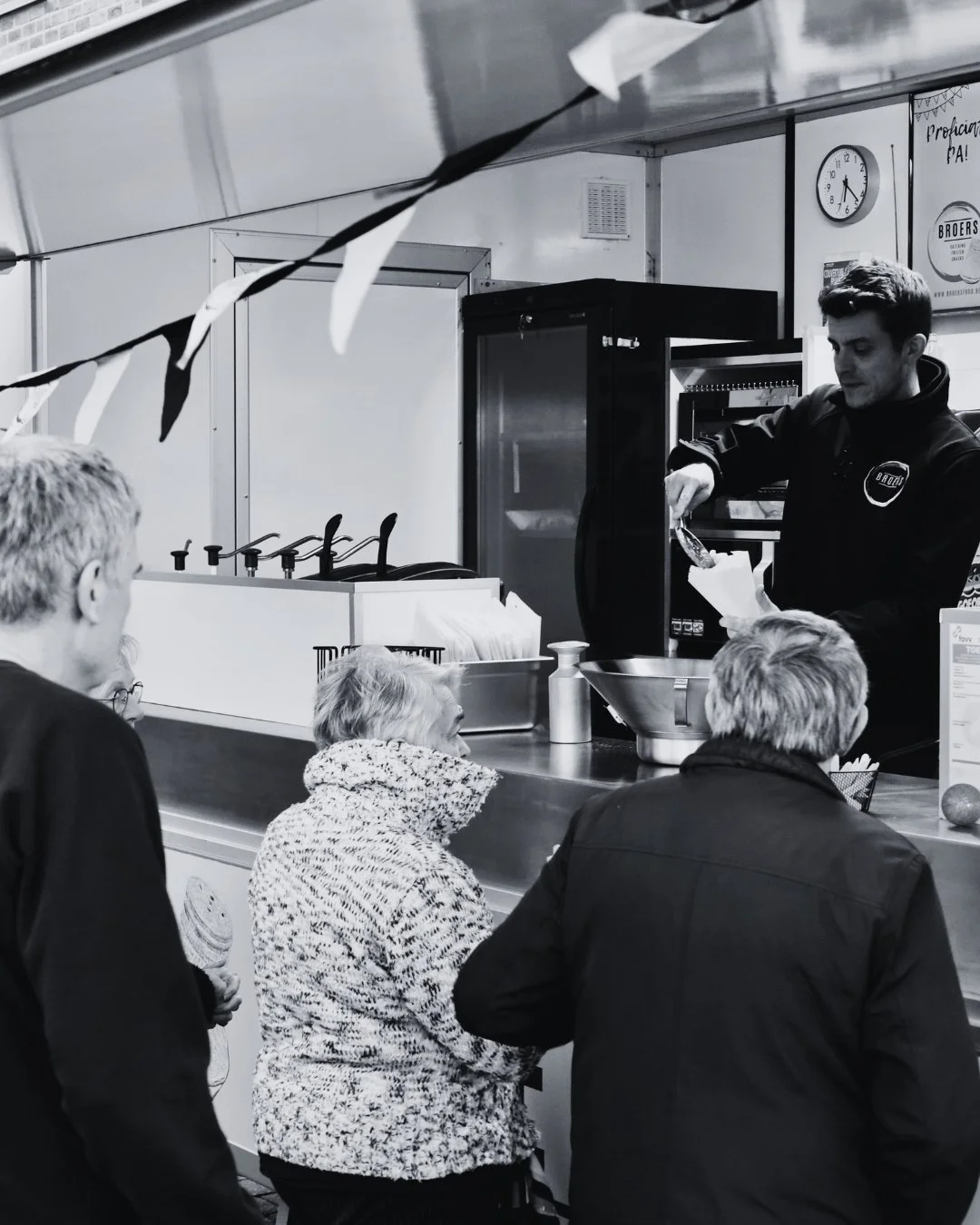 Een man serveert voedsel aan een rij van oudere mensen aan een kraam op een markt of evenement.