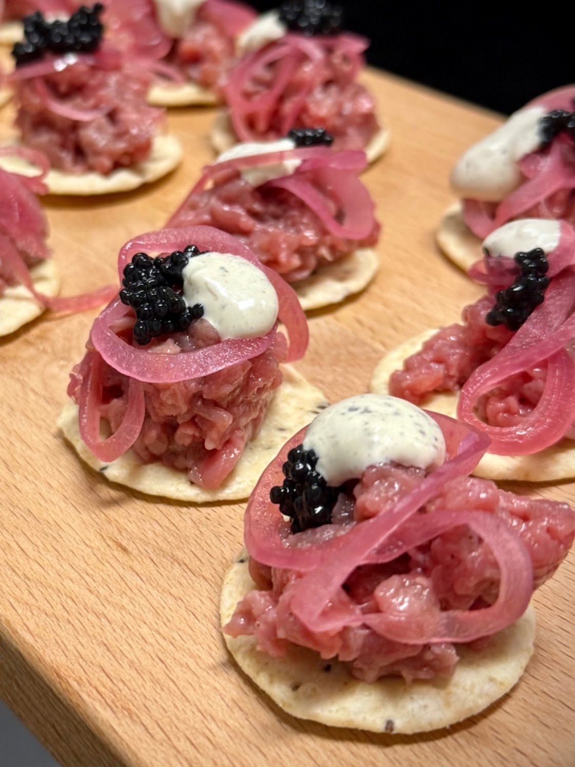 Hapjes met rauwe hertenvlees, rode ui en zwarte kaviaar op een ronde cracker.