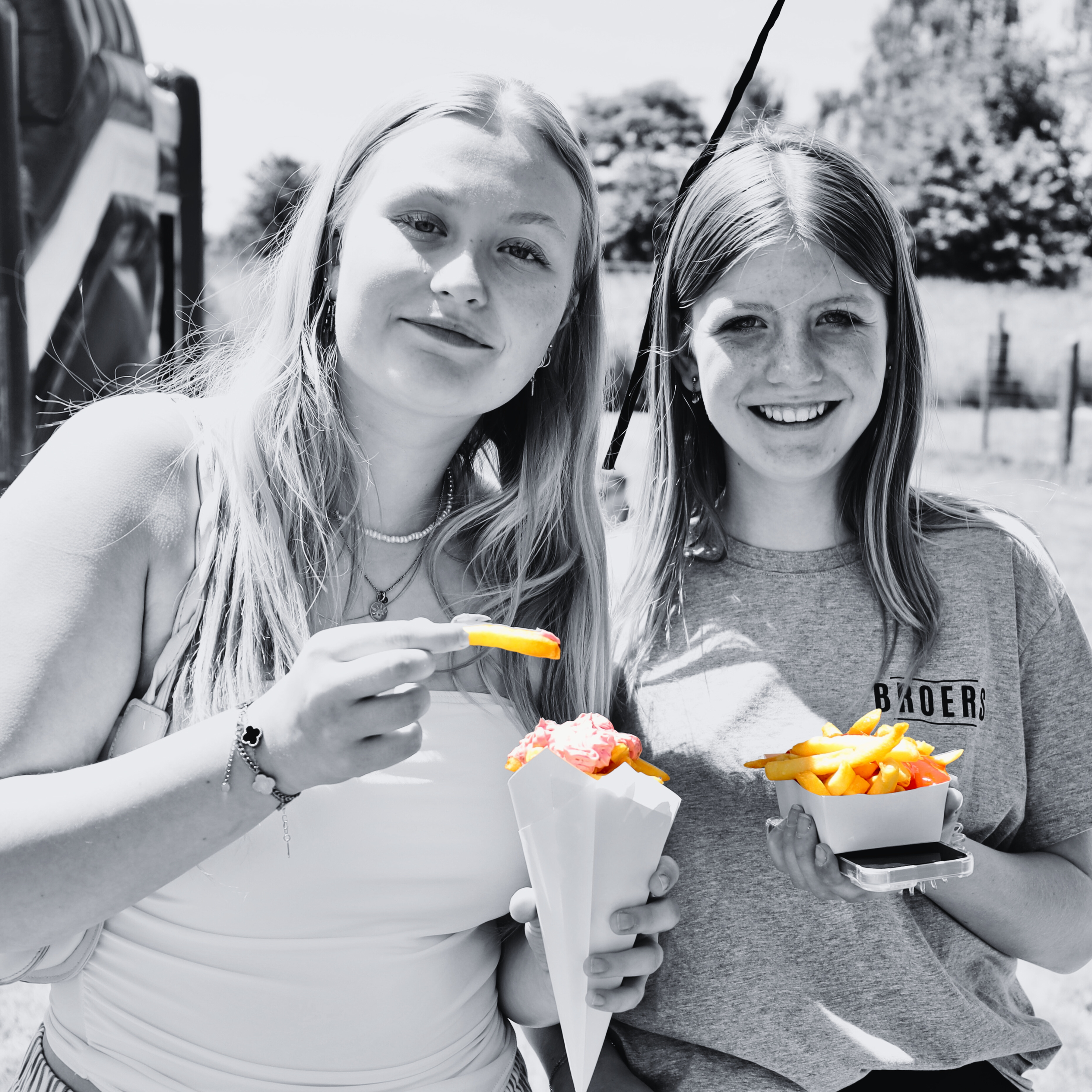 Twee tienermeisjes genieten van ijsjes en friet tijdens een zonnige dag op het platteland.