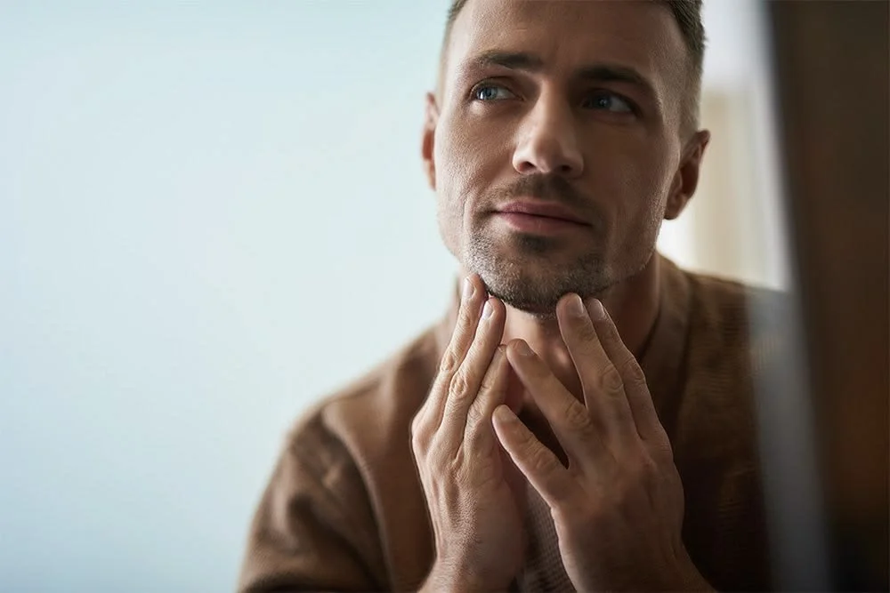 A man touching his jawline and chin, looking thoughtfully to the side.
