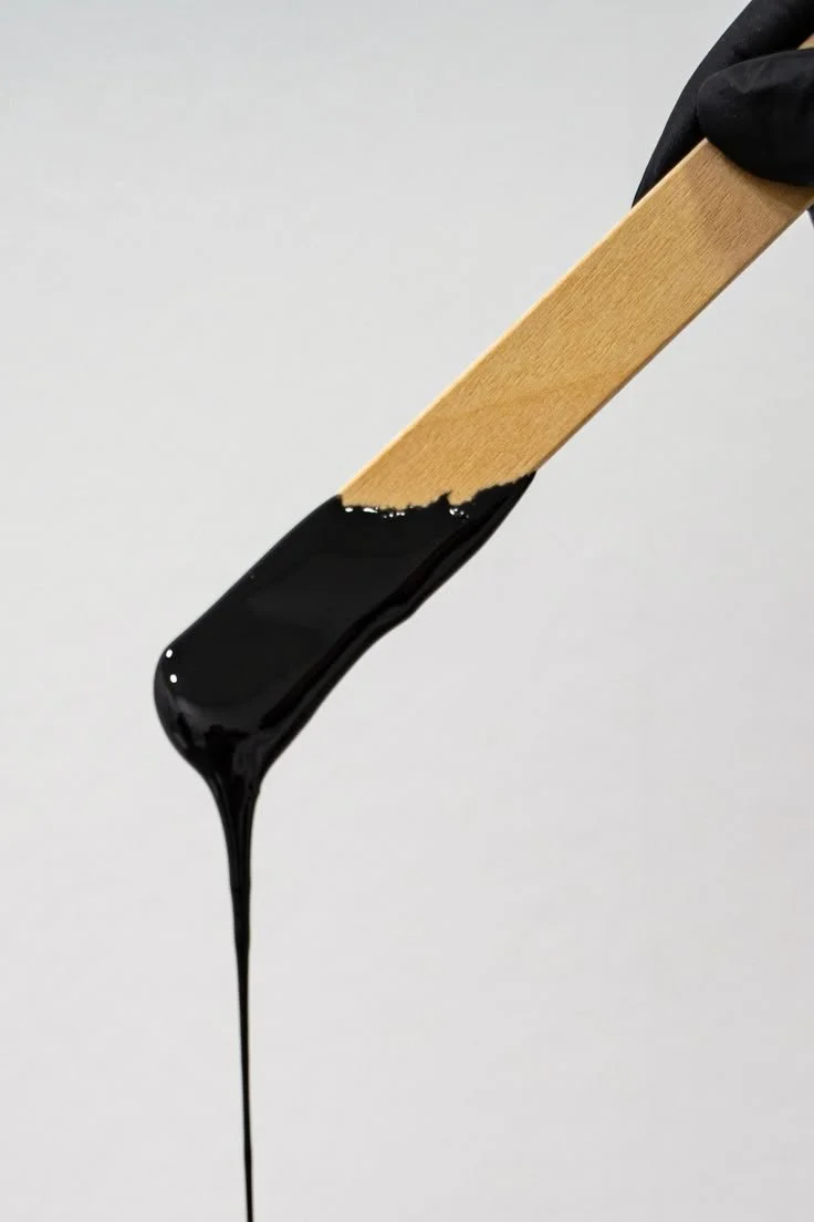 A paintbrush with black paint dripping from its bristles.