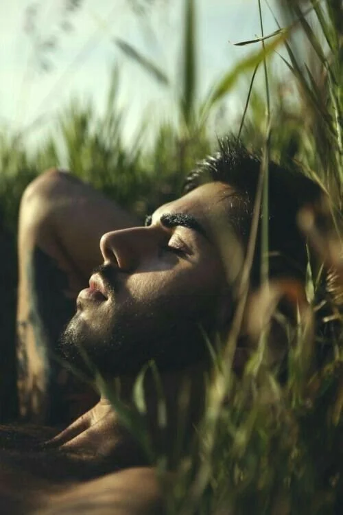 A man lying in tall grass with eyes closed, basking in sunlight.
