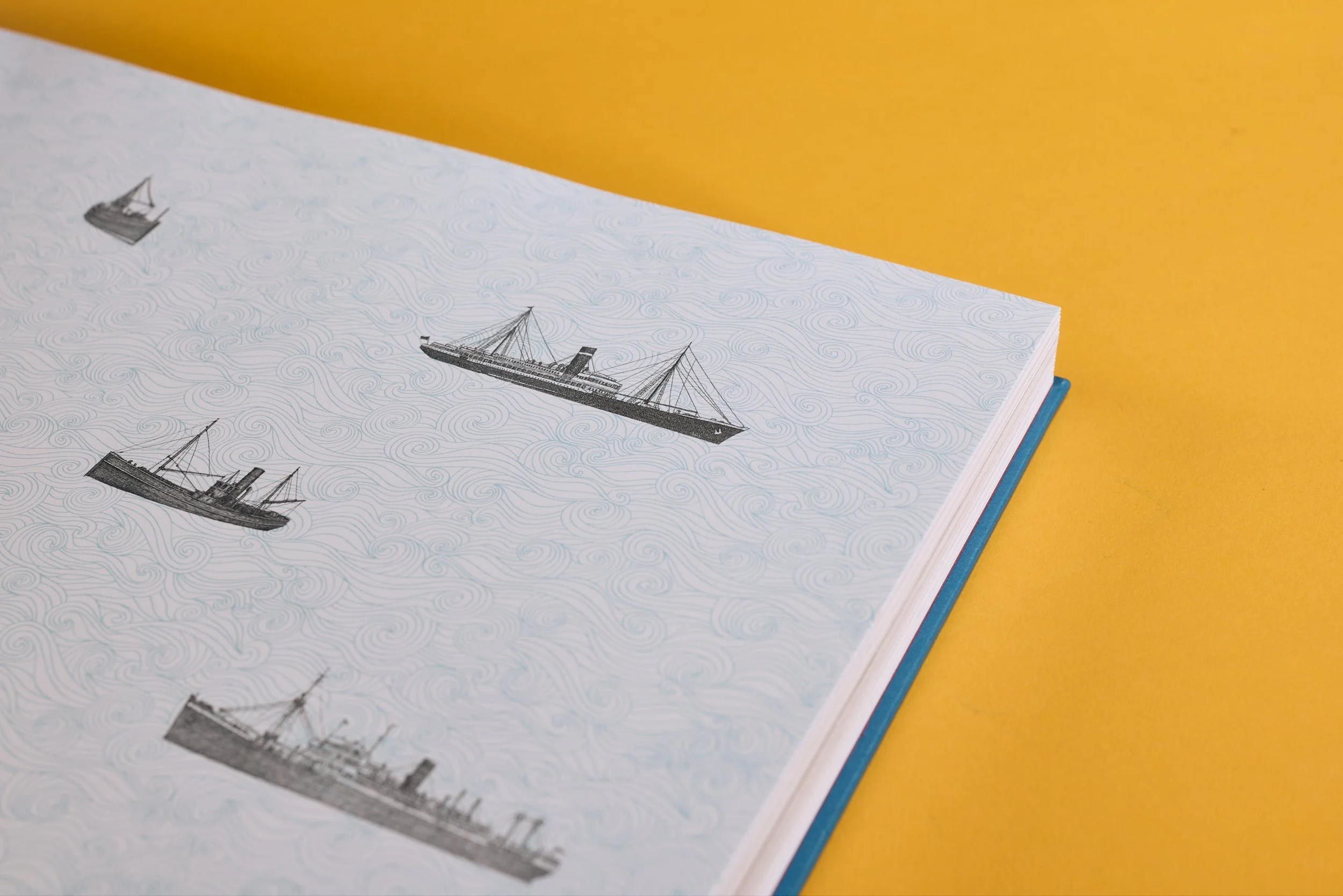Close-up of a Book with black ship illustrations on a patterned background, with a yellow surface in the background.